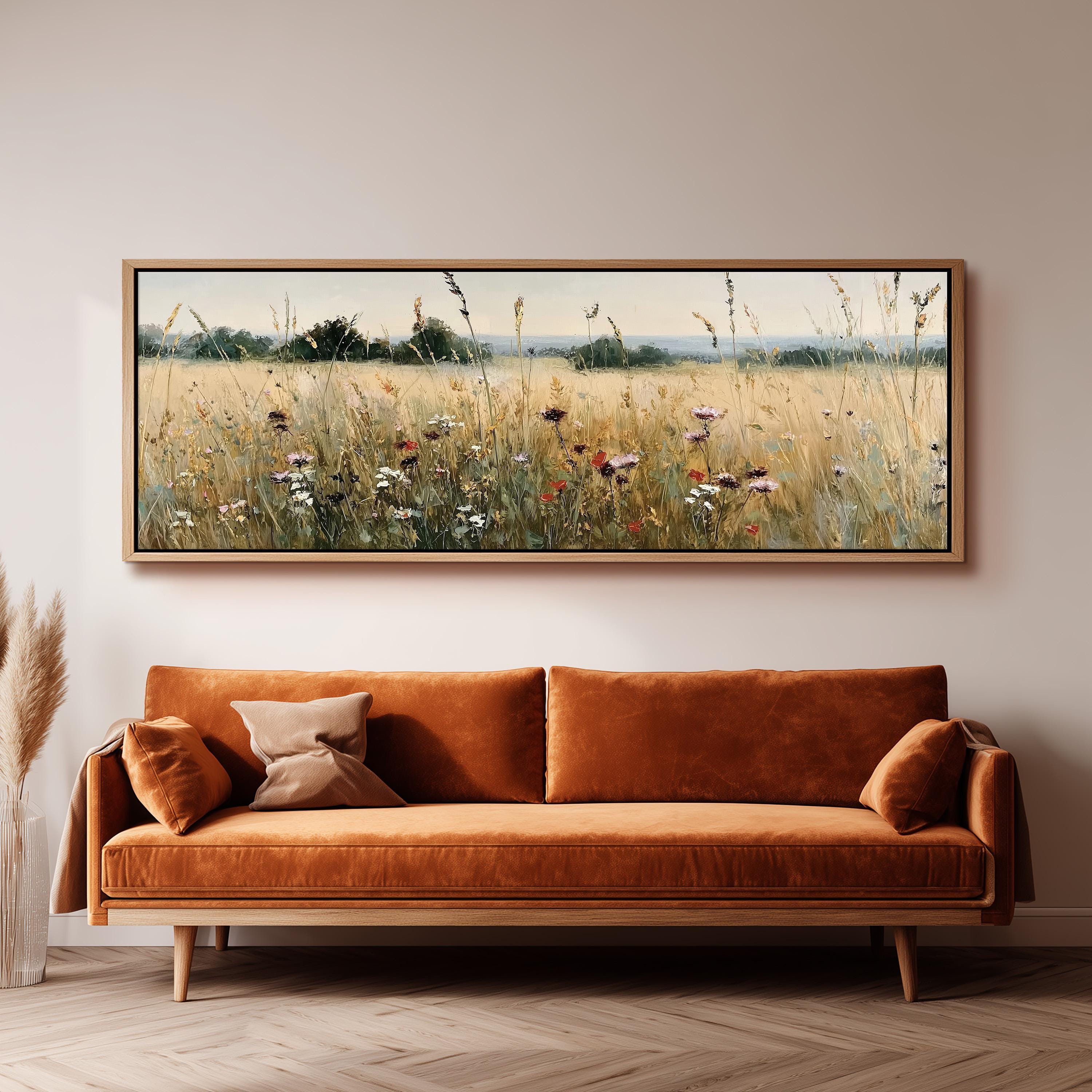 a large, framed painting of a field with tall grass and wildflowers hanging on a wall above a brown sofa.