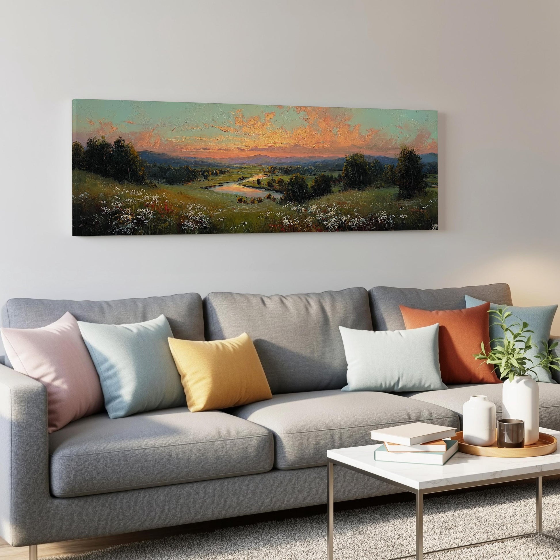a large landscape painting hanging on a wall above a gray couch with colorful throw pillows. The painting depicts a serene countryside scene with a winding river and lush greenery.