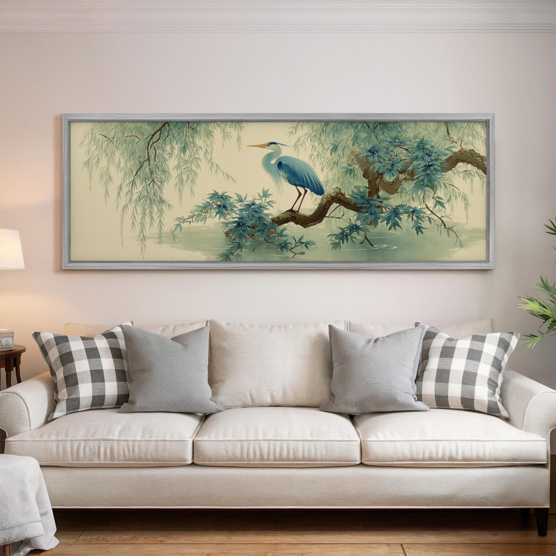 a large framed painting of a blue heron perched on a branch, hanging on a wall above a white sofa with gray and white patterned pillows.
