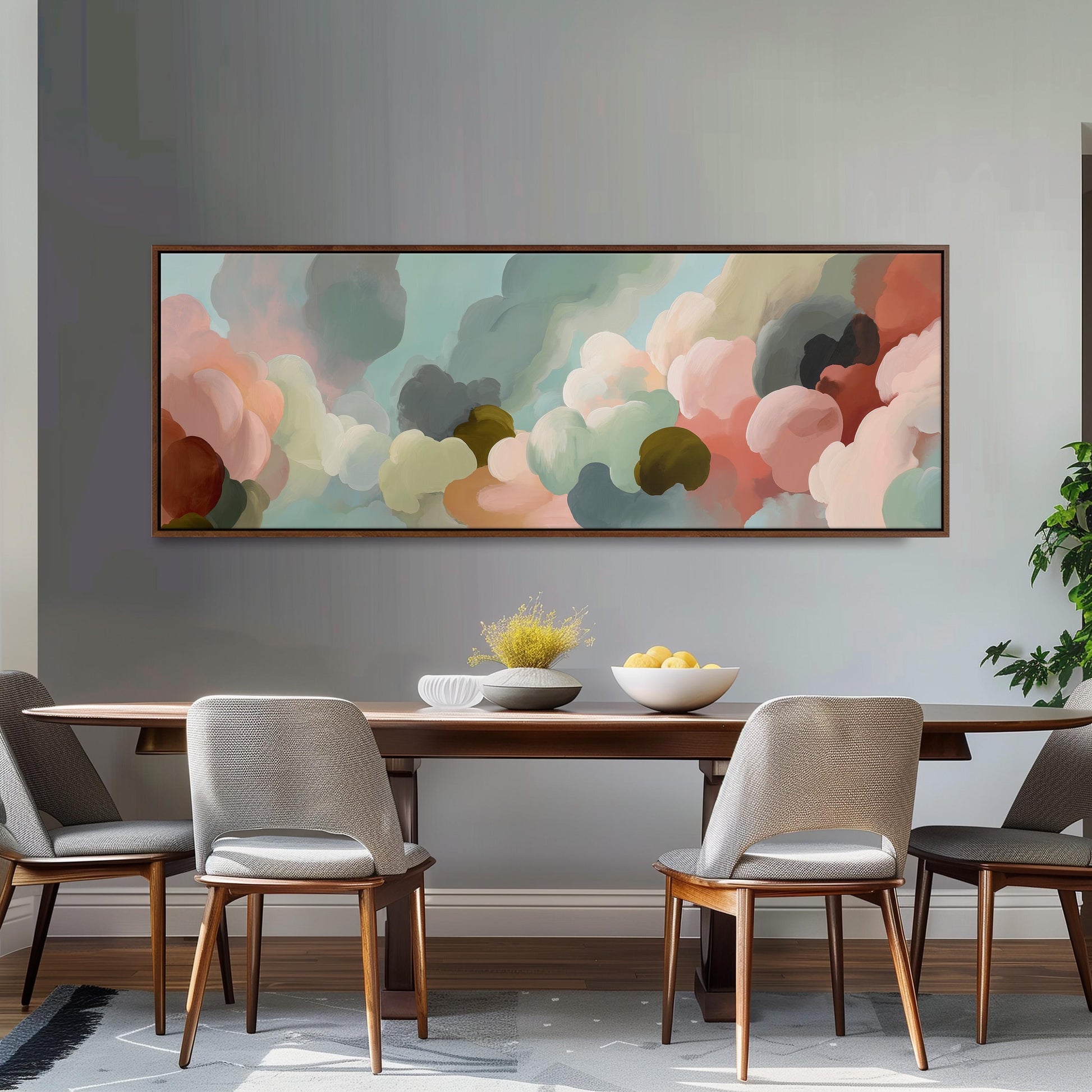 a dining room with a large abstract painting hanging on the wall above a wooden table with four chairs. The painting has a colorful, cloud-like design with shades of pink, blue, and green. The table is set with a bowl of fruit and a vase of flowers, creating a cozy and inviting atmosphere.