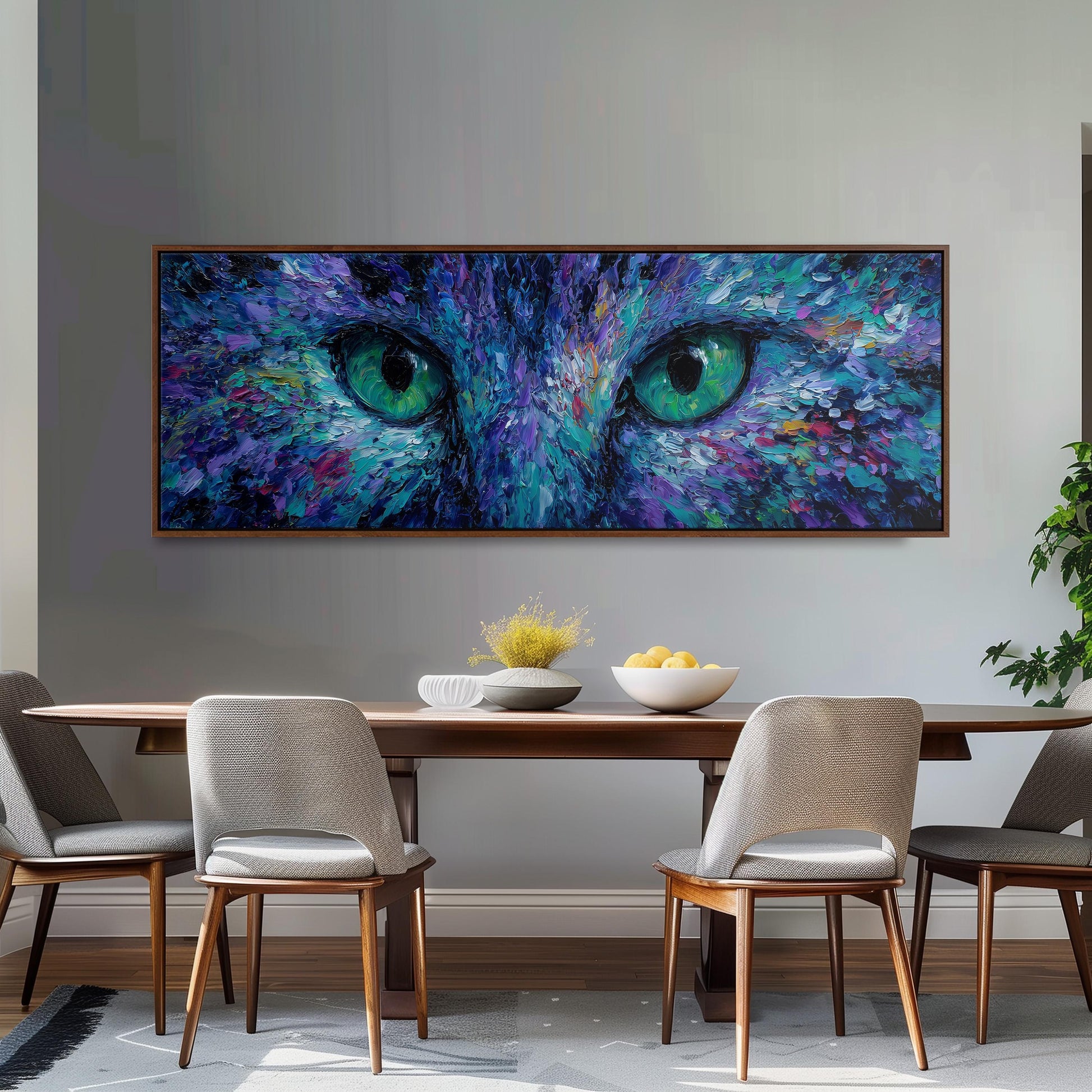 a large painting of a cat's face with striking blue and green eyes, hanging on a wall above a wooden dining table with four chairs.