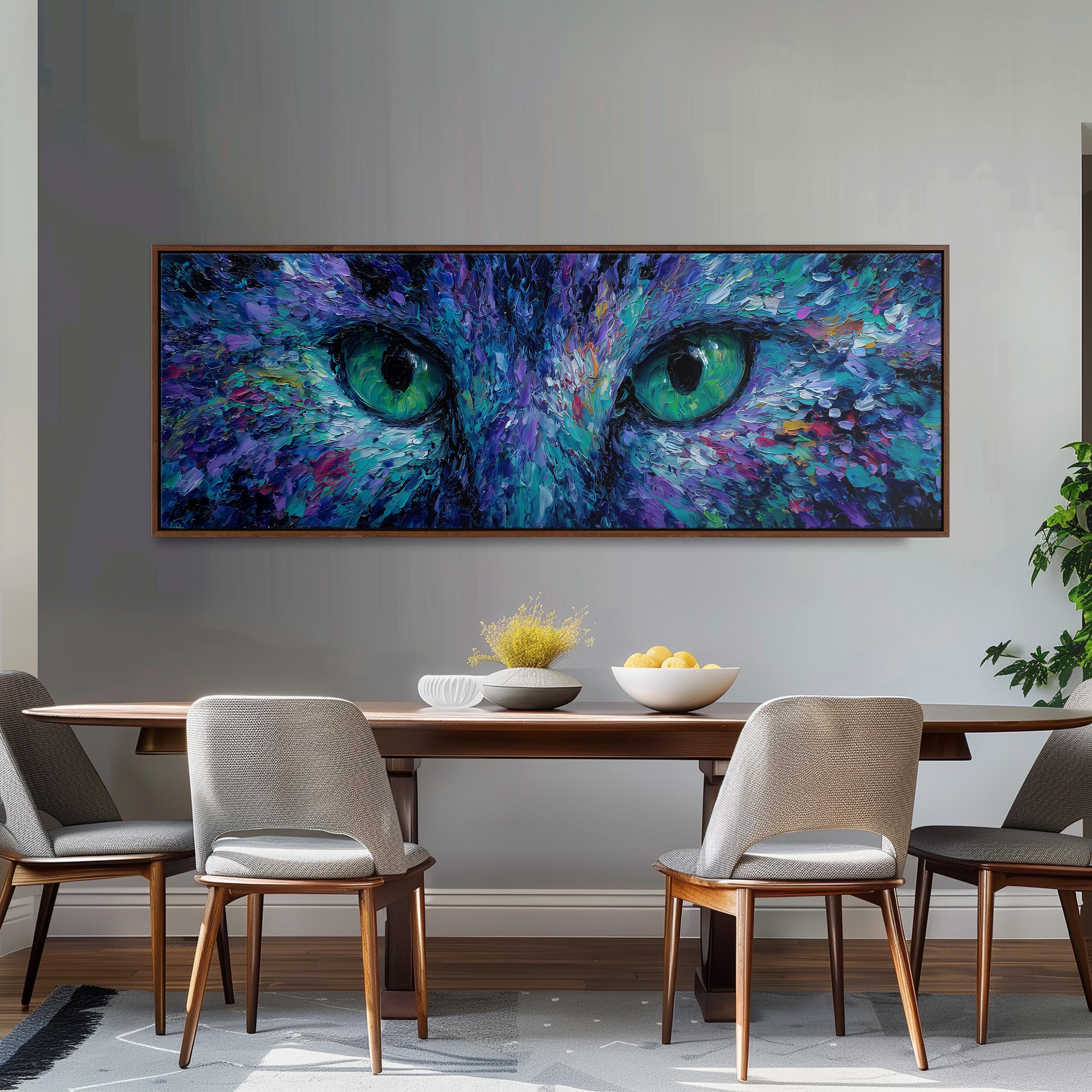 a large painting of a cat's face with striking blue and green eyes, hanging on a wall above a wooden dining table with four chairs.