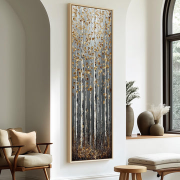 a large, framed painting of a forest scene with tall trees and a mix of brown and white colors. The painting is hanging on a white wall, and there are two chairs and a small table in the foreground.
