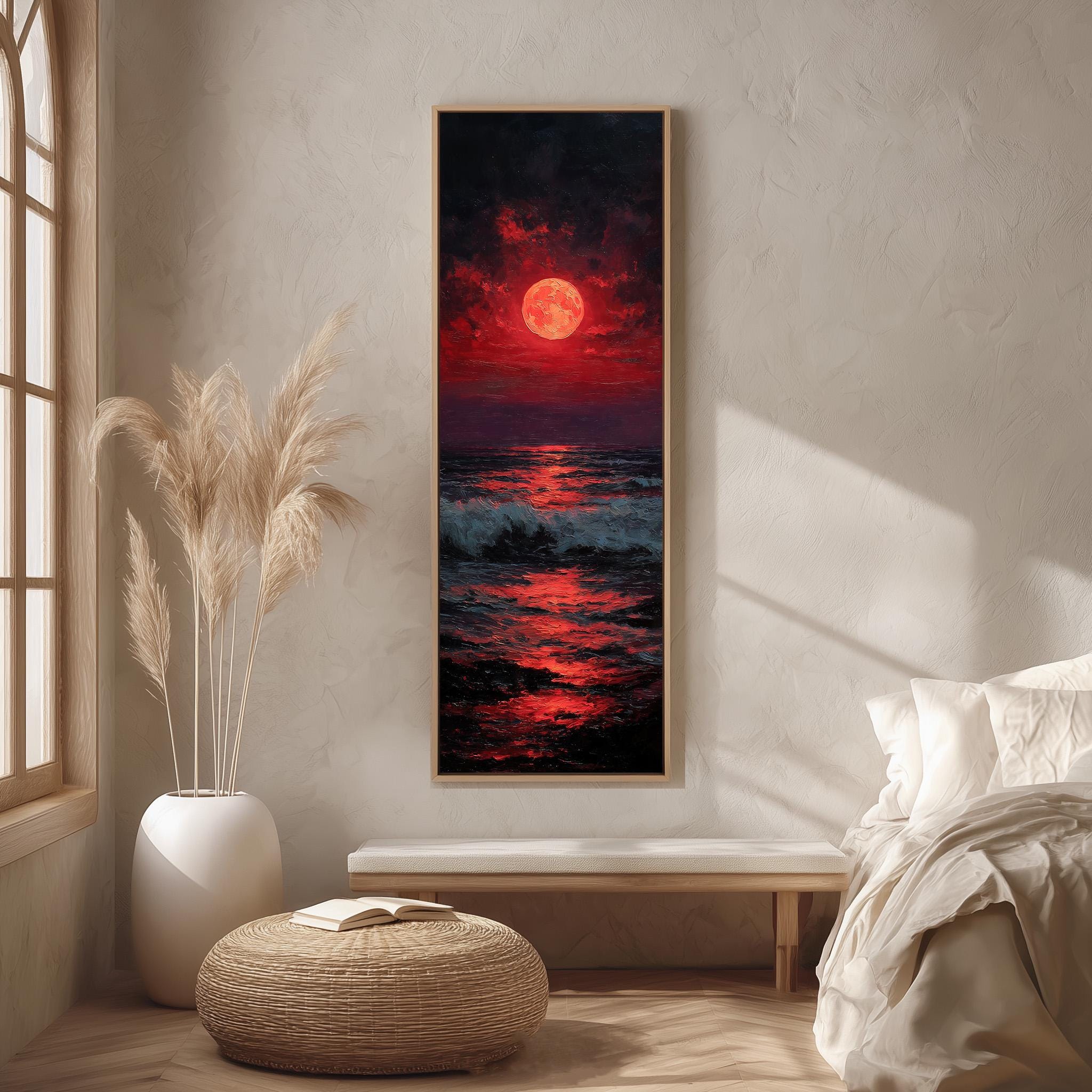 a large painting of a sunset over the ocean, with a large red moon in the sky. The painting is hanging on a wall in a room with a bed, a potted plant, and a woven ottoman.