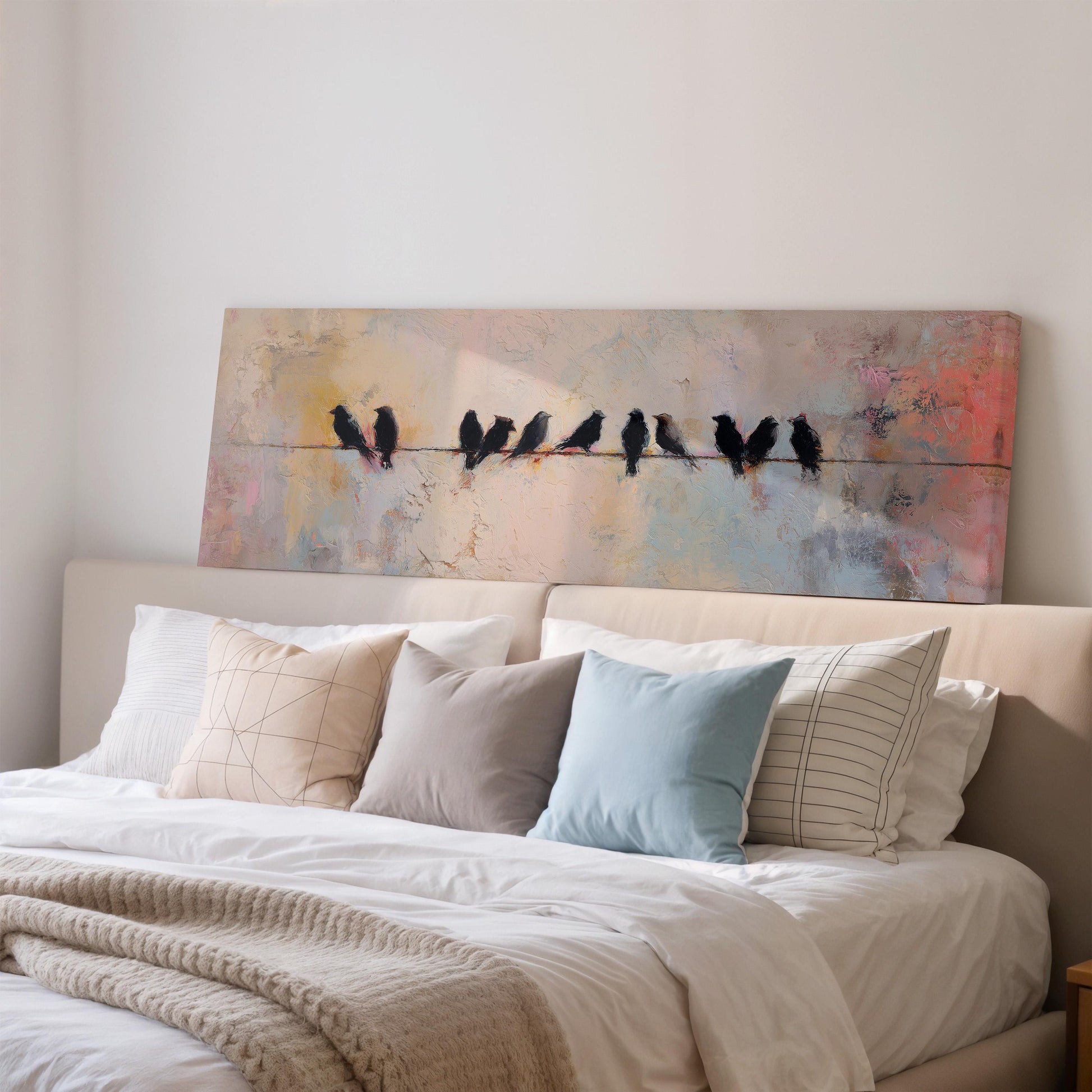 a large painting of birds perched on a wire above a bed with white pillows and a gray blanket.