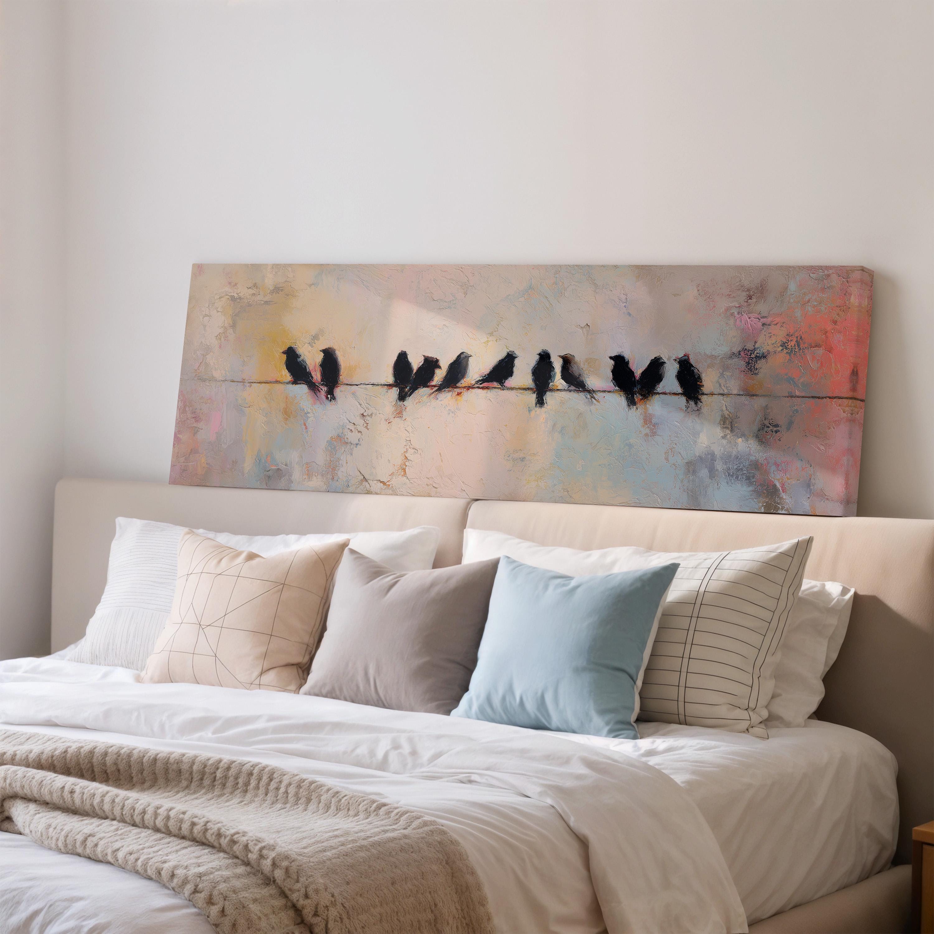 a large painting of birds perched on a wire above a bed with white pillows and a gray blanket.