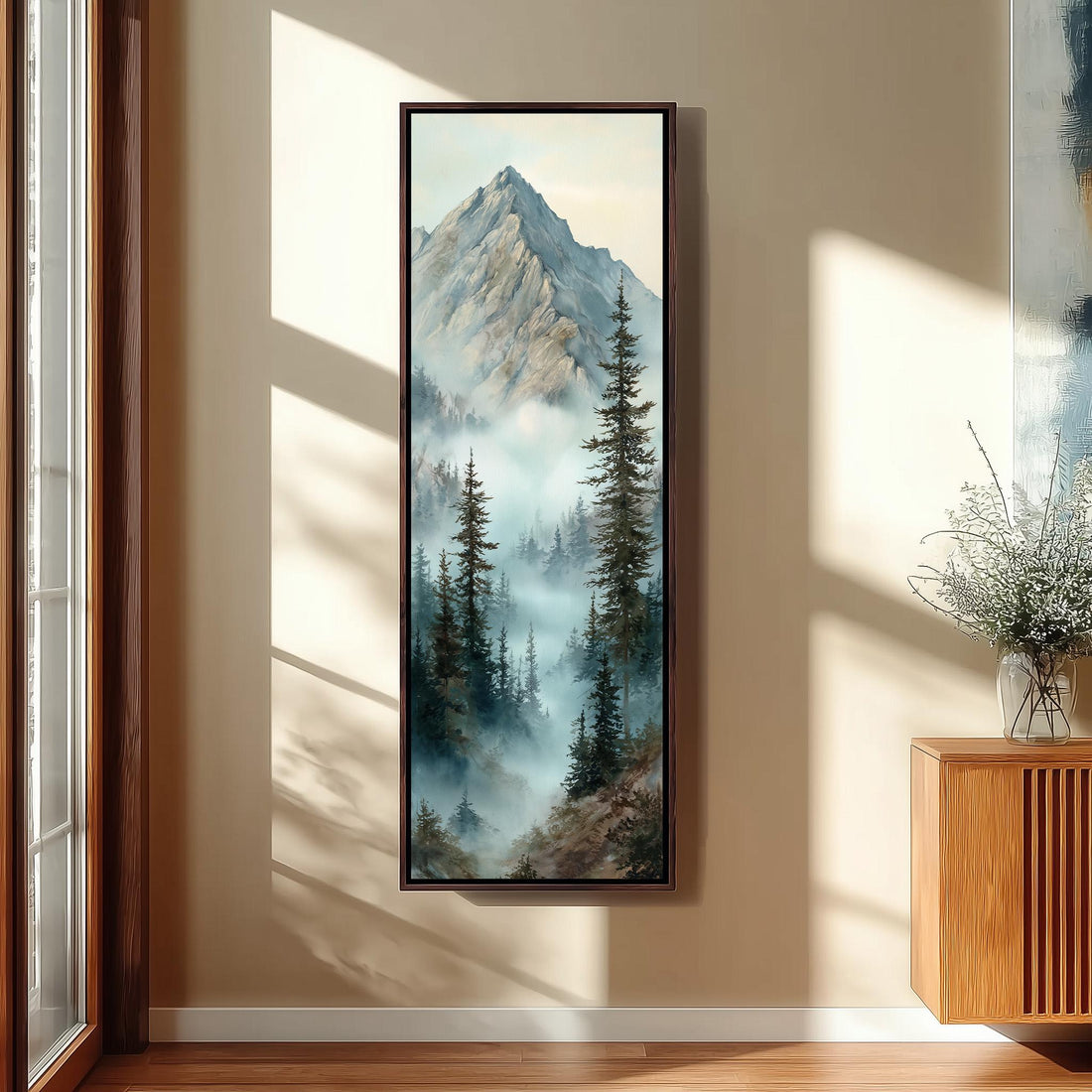 a large framed painting of a mountain landscape with pine trees and a misty, hazy atmosphere. The painting is hanging on a wall in a room with a wooden floor and a window.