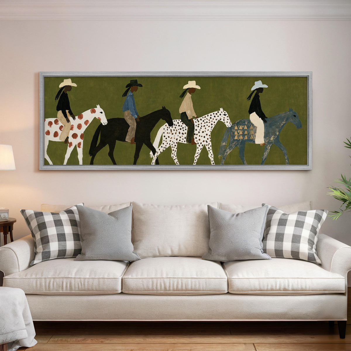 Riders on spotted ponies on olive green panoramic canvas print above a white sofa in a bright living room