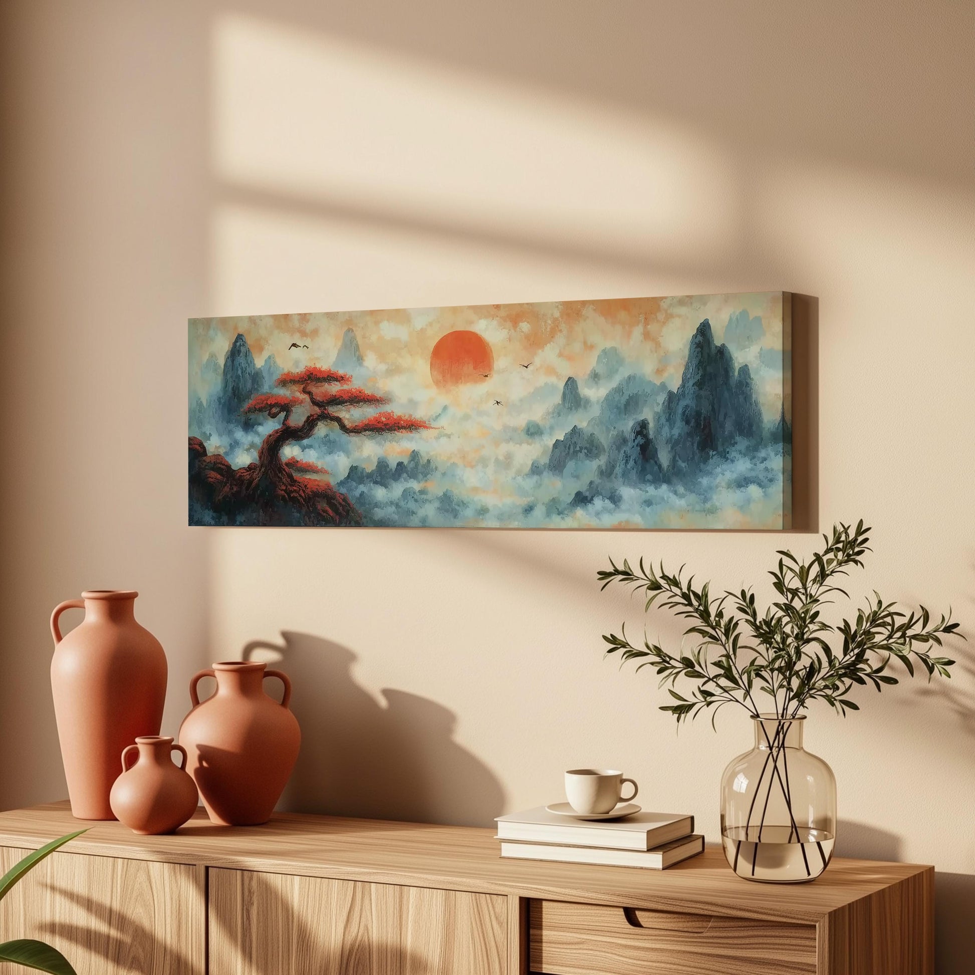 a wooden cabinet with a painting of a landscape hanging on the wall above it. The painting depicts a serene scene with a tree, mountains, and a red sun in the sky. The cabinet also has three orange vases, a white coffee cup, and a stack of books on top.
