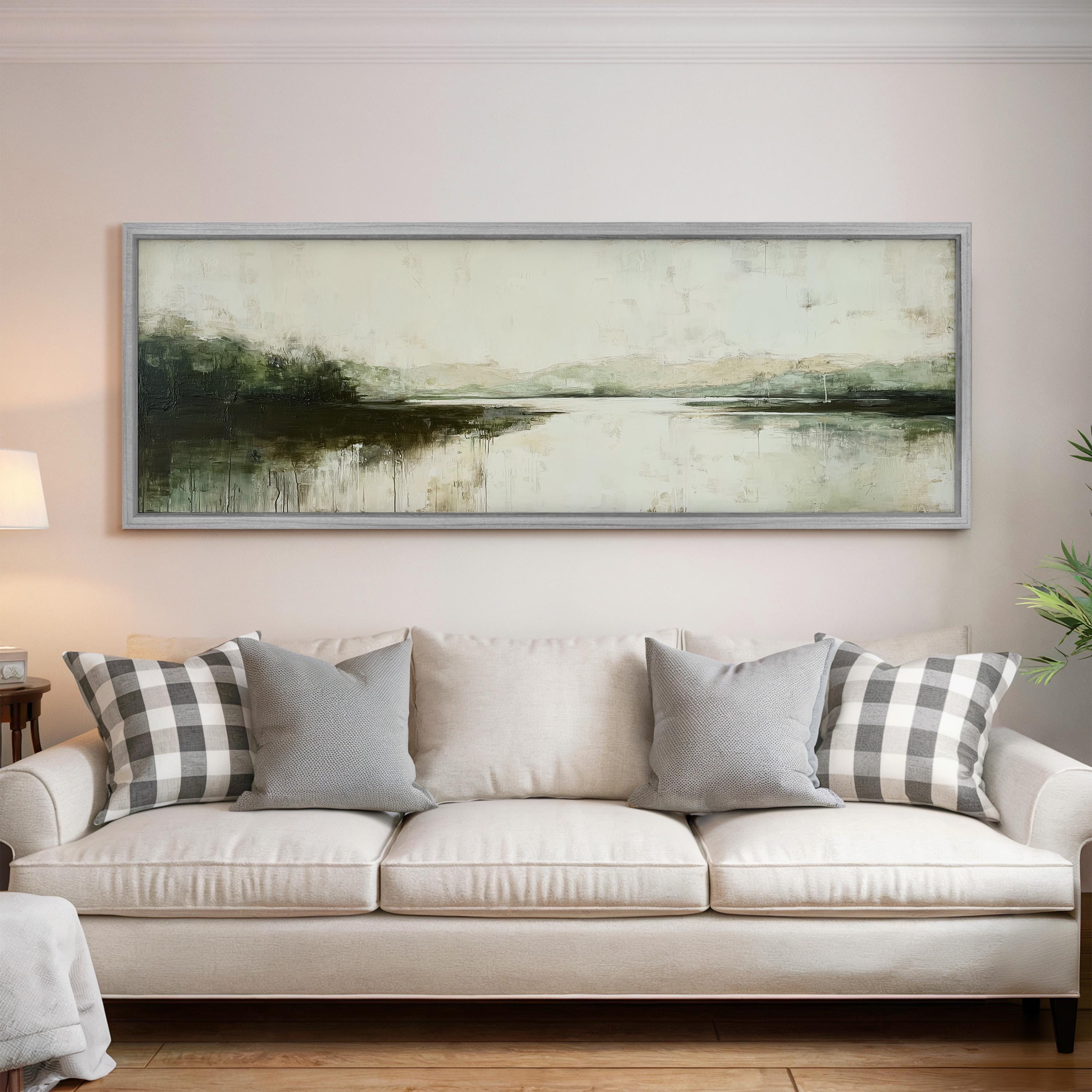 a living room with a large, framed landscape painting hanging on the wall above a white sofa with gray and white patterned throw pillows.