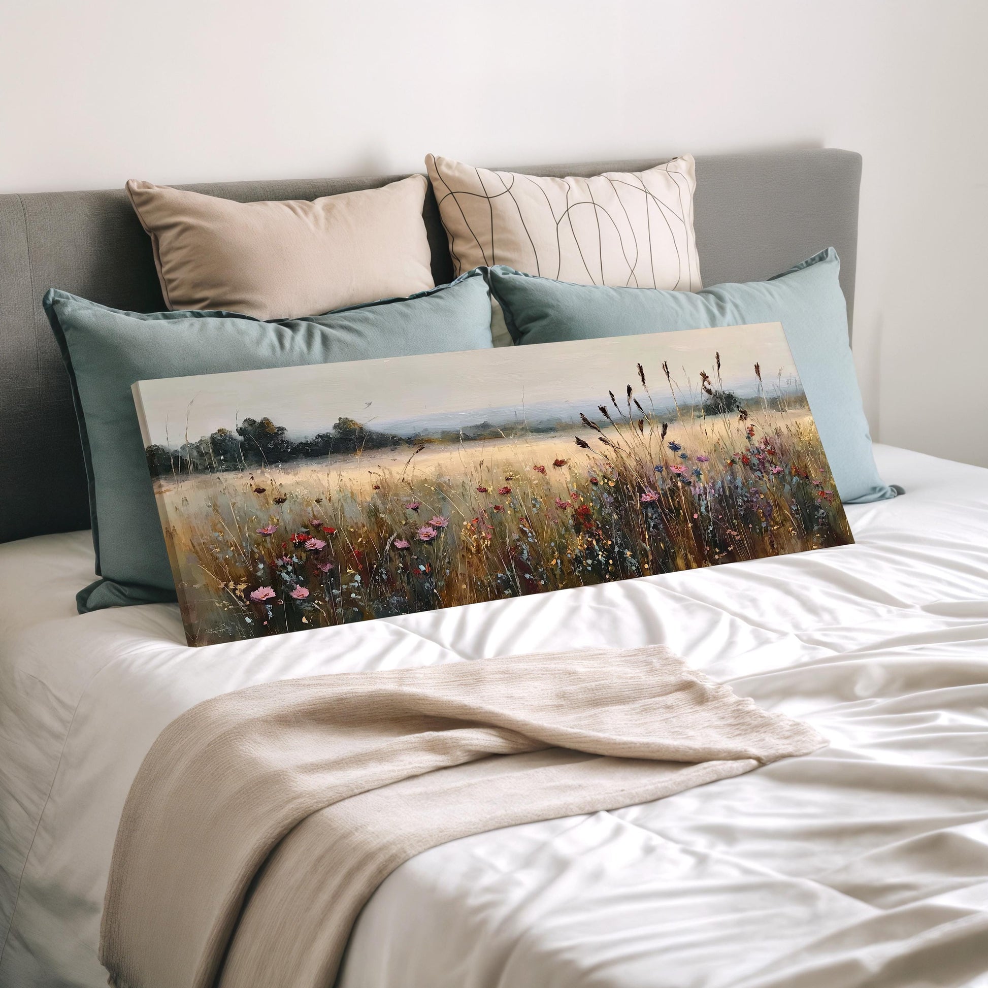 a bedroom with a bed and a painting of a field of flowers on it. The bed is covered with a white comforter and has several pillows on it. The painting is placed on the bed, and the bed is positioned against a wall.