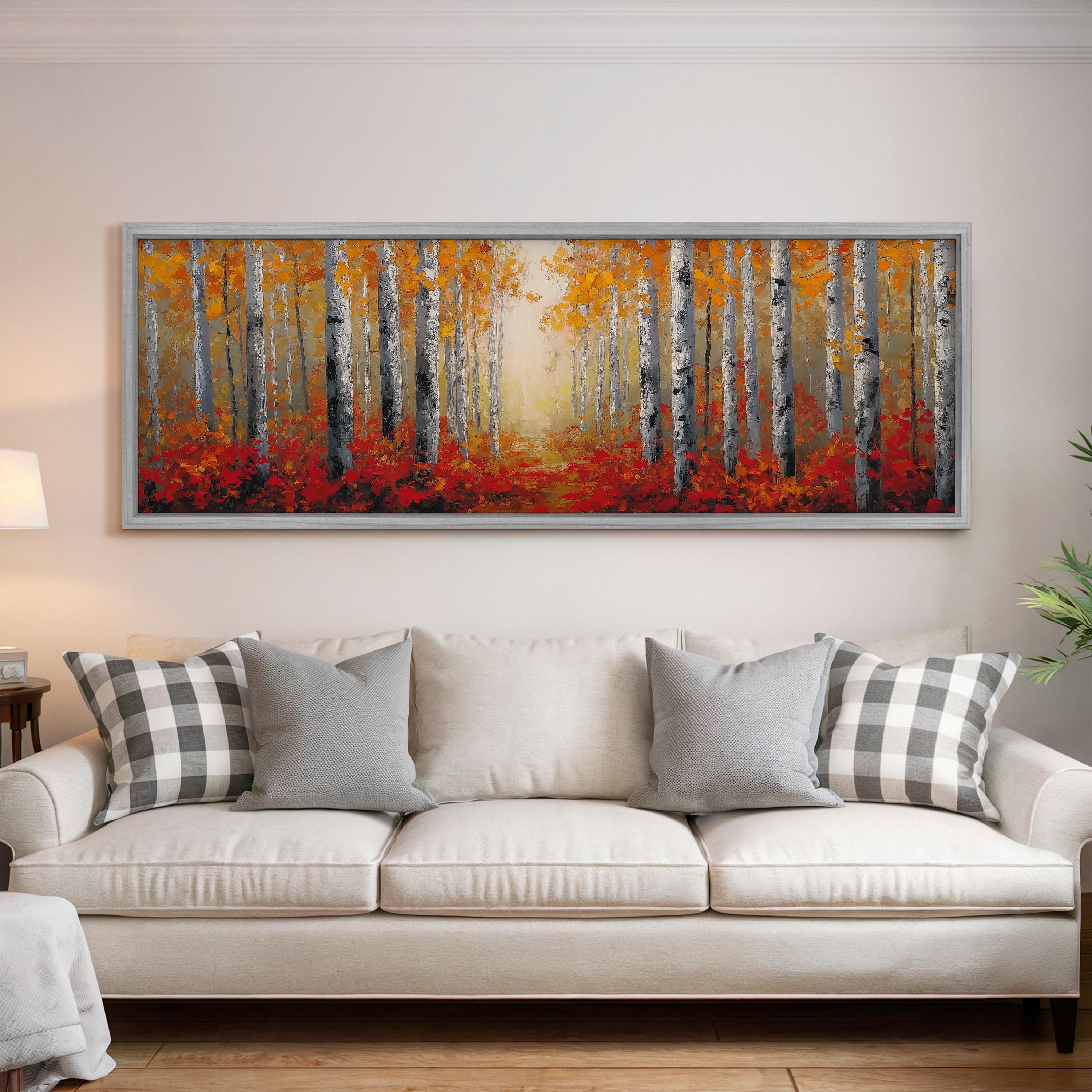 a large, framed painting of a forest with tall trees and vibrant orange and red foliage, hanging on a wall above a white couch with gray and white patterned pillows.