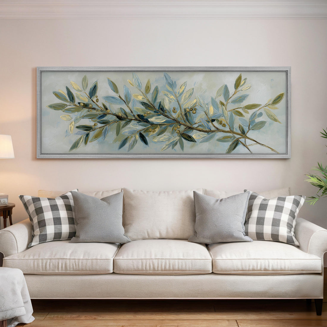 a large, framed painting of a branch with green leaves and small white flowers hanging above a white couch with gray and white plaid throw pillows.