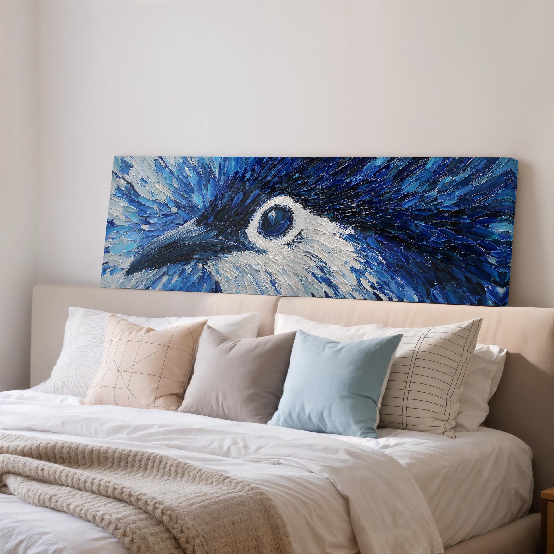 a large, colorful painting of a blue bird's head hanging above a bed with white pillows and a beige blanket.