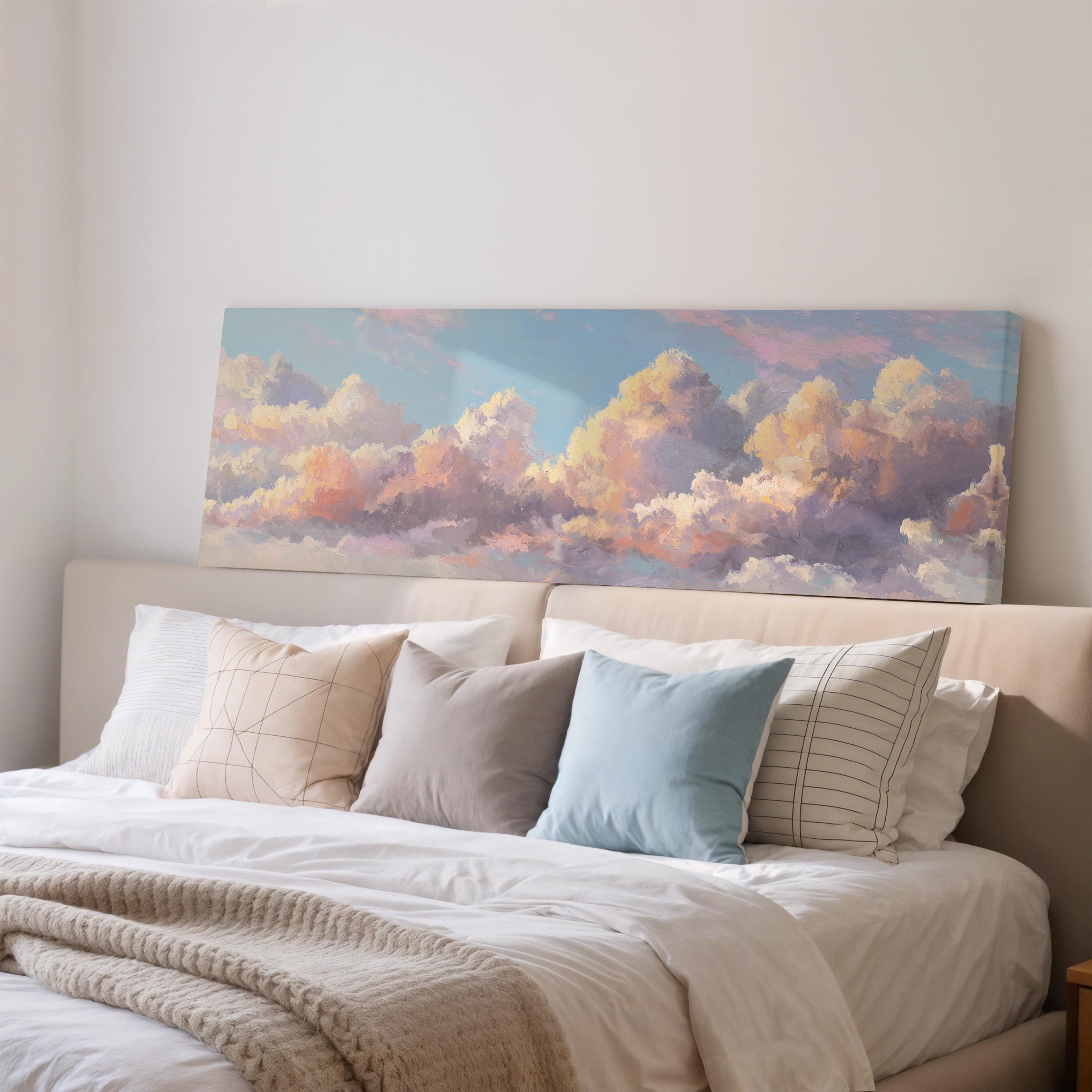 a large painting of a cloudy sky hanging above a bed with white pillows and a gray blanket.