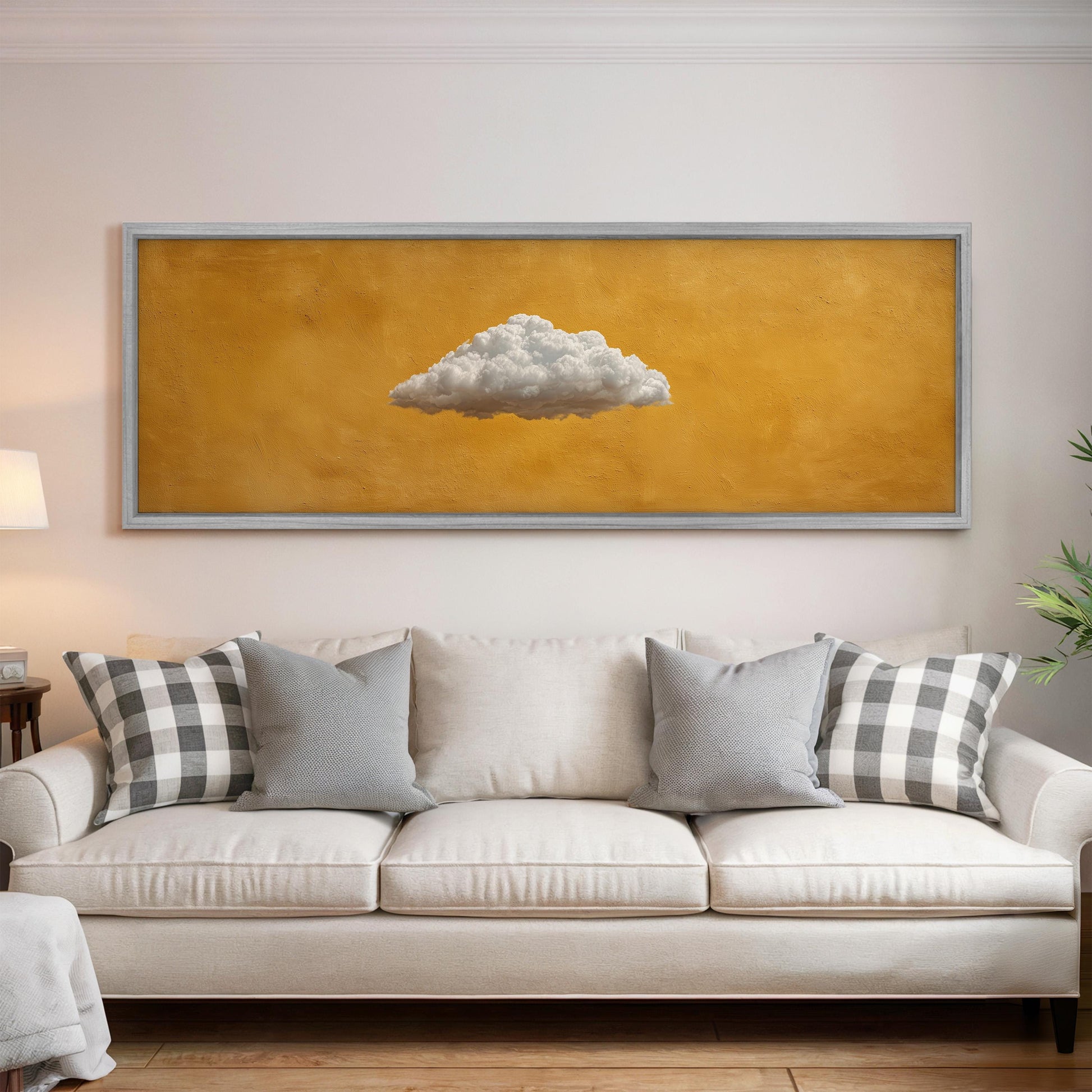 a large, framed painting of a cloud hanging on a wall above a white couch with gray and white plaid throw pillows.