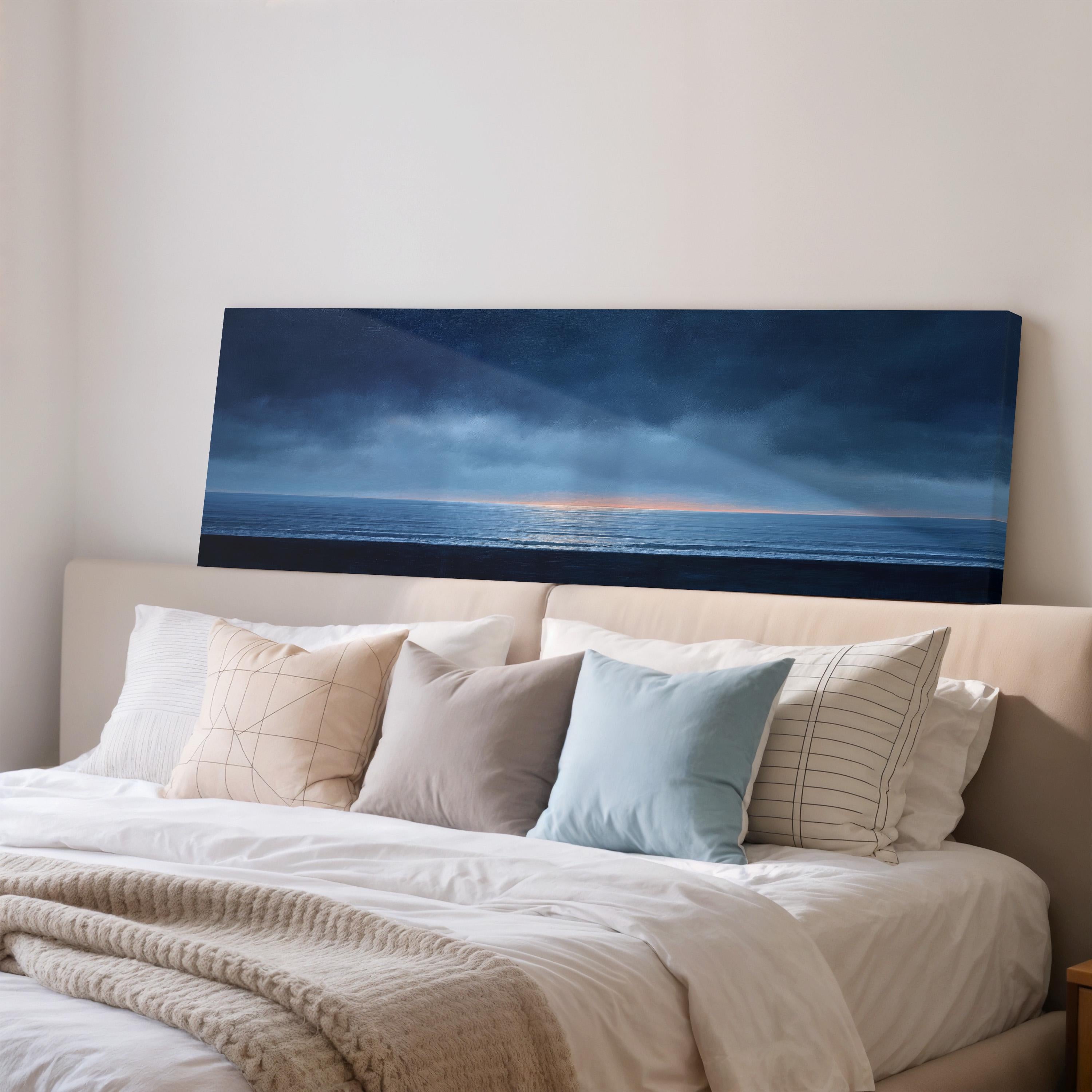 a bedroom with a large bed covered in white sheets and pillows. Above the bed, there is a large canvas print depicting a serene ocean scene with a cloudy sky.