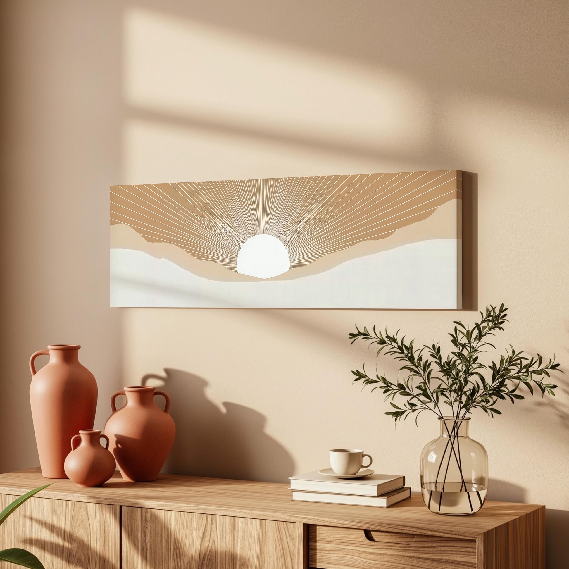 a wooden cabinet with a vase of greenery, a coffee cup, and a stack of books on top. Above the cabinet, there is a framed artwork depicting a sun-like design.