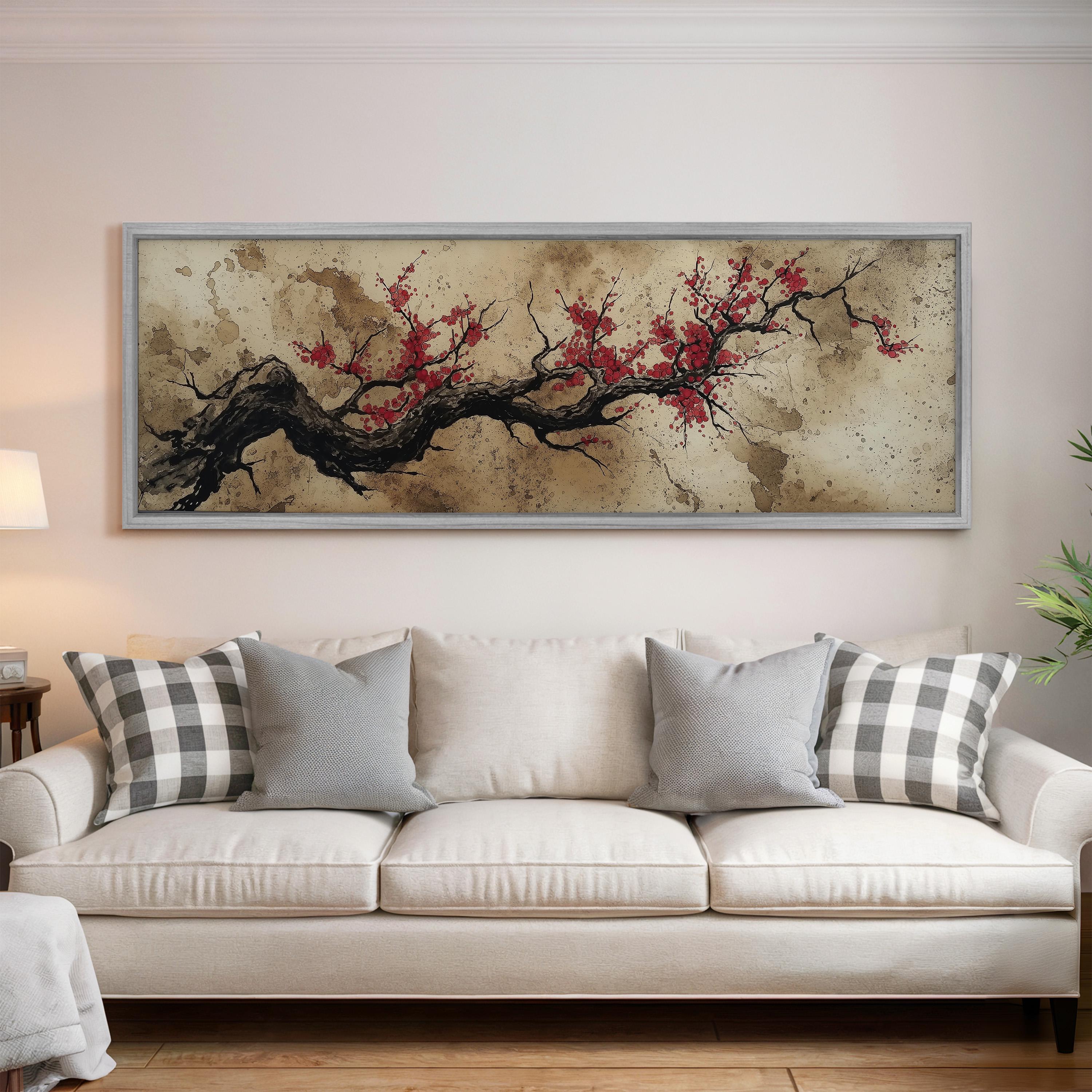 a large, framed painting of a tree branch with red flowers hanging above a white couch in a living room setting.