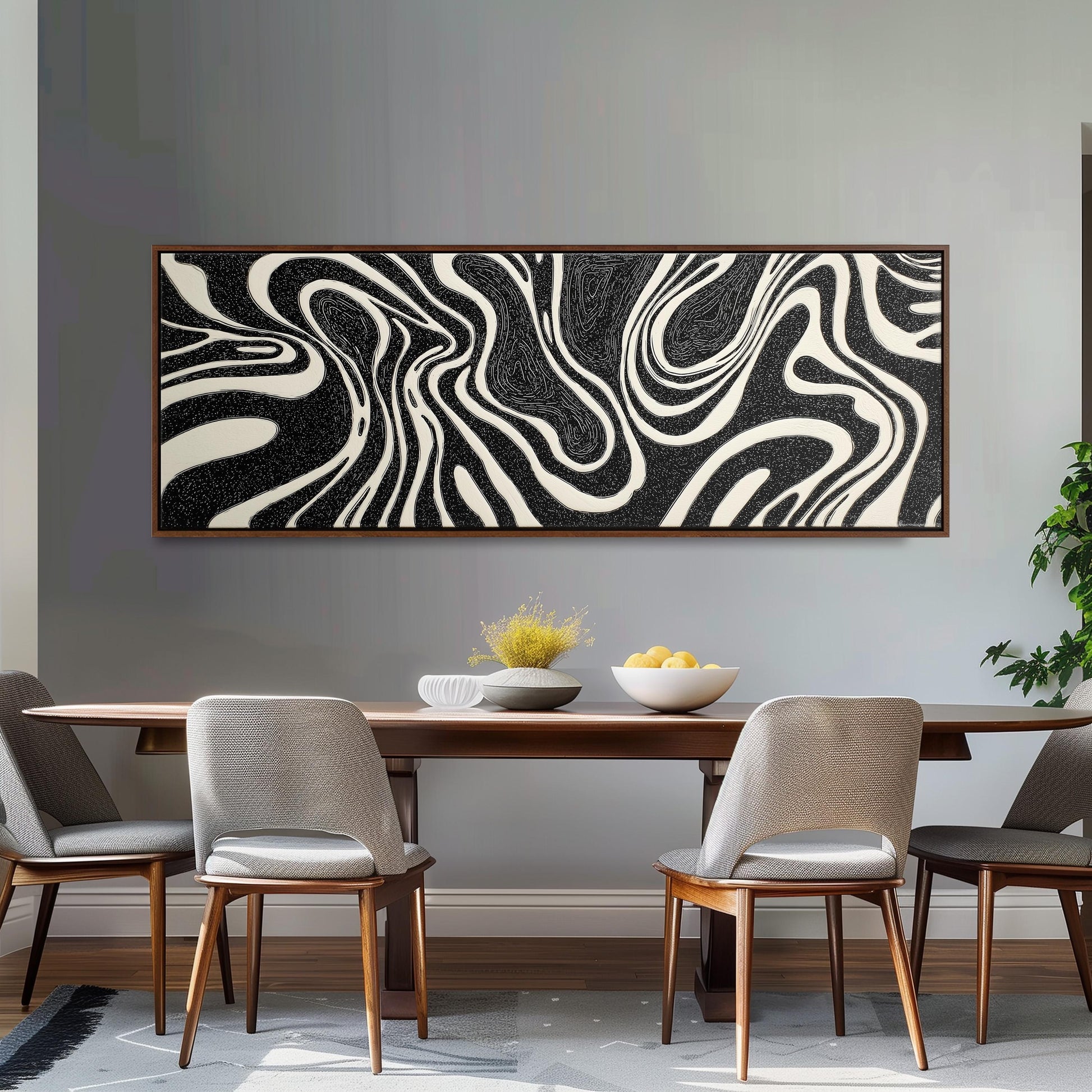 a modern dining room with a wooden table and four gray chairs. Above the table, there is a large abstract painting with black and white swirls and lines. On the table, there is a bowl of fruit and a vase of flowers.