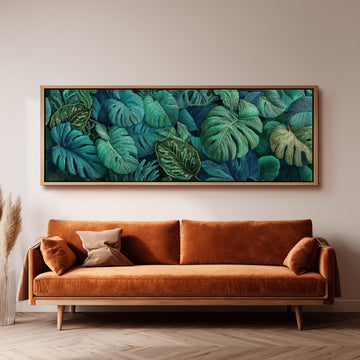 a large, framed painting of tropical leaves hanging on a wall above a brown sofa.