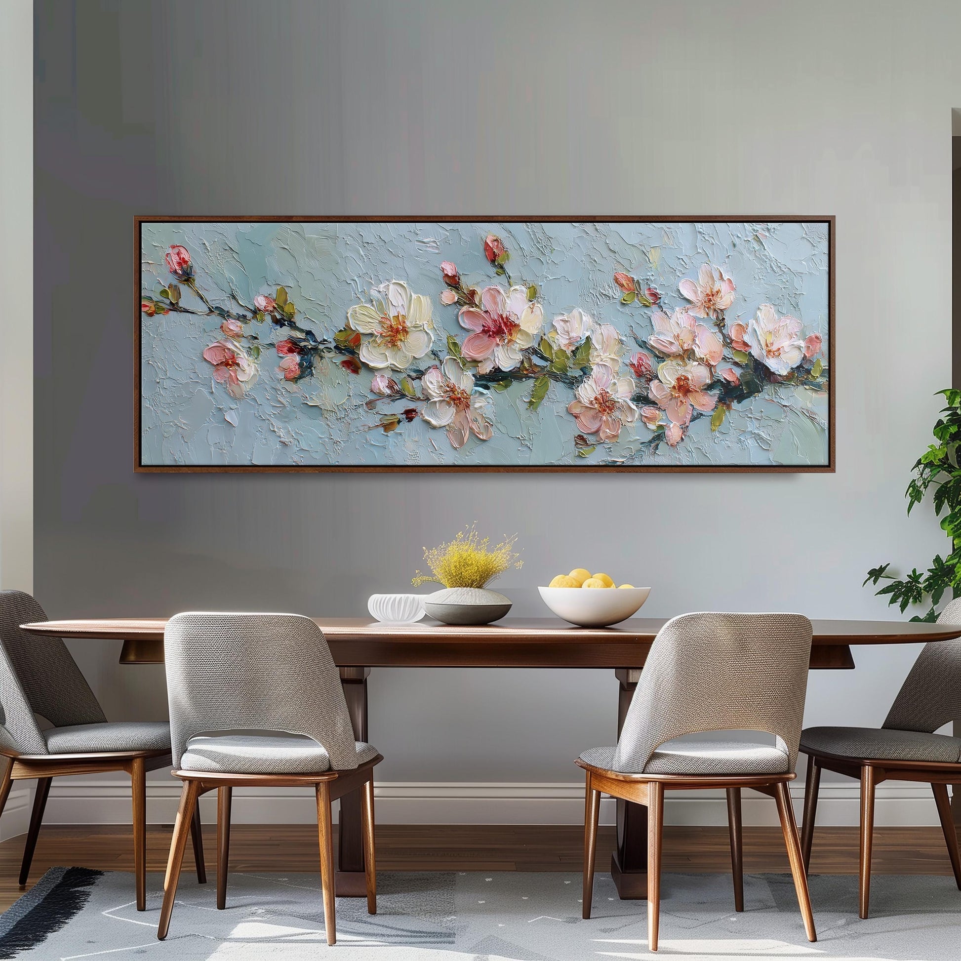 a dining room with a large painting of pink flowers hanging on the wall above a wooden table with four chairs. The table is set with a bowl of fruit and a vase of flowers, creating a cozy and inviting atmosphere.