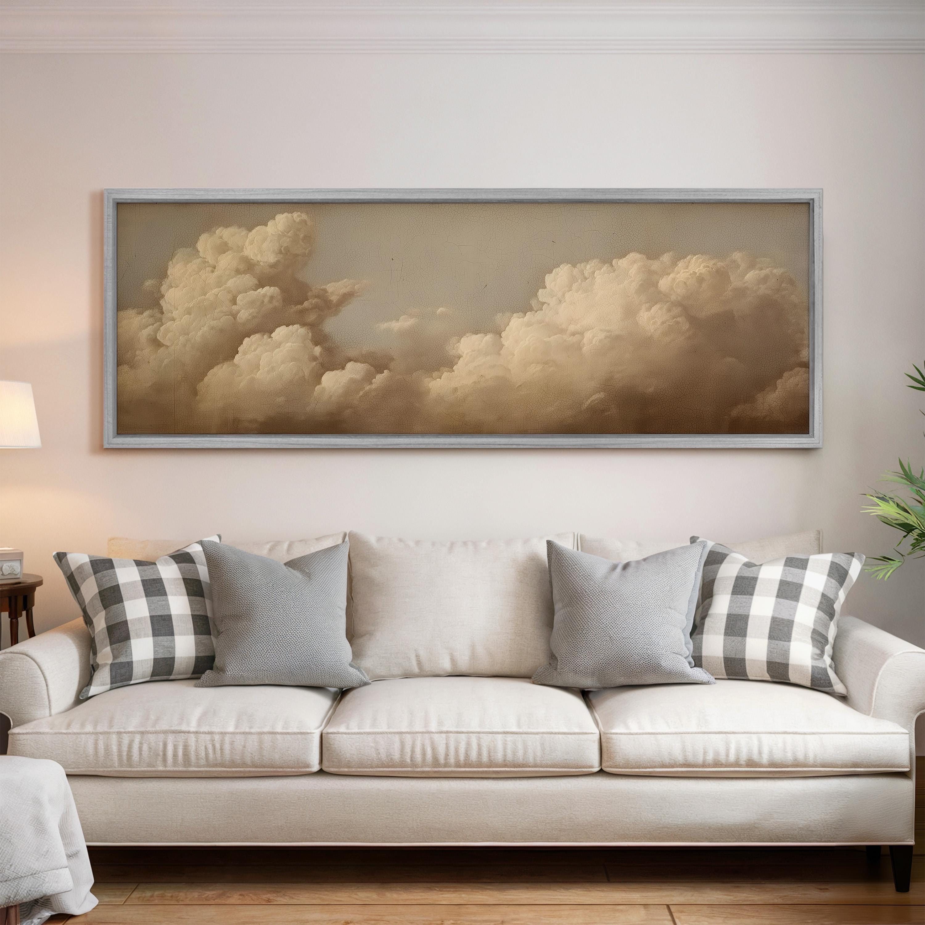a large framed painting of a cloudy sky hanging above a white sofa with gray and white plaid throw pillows.