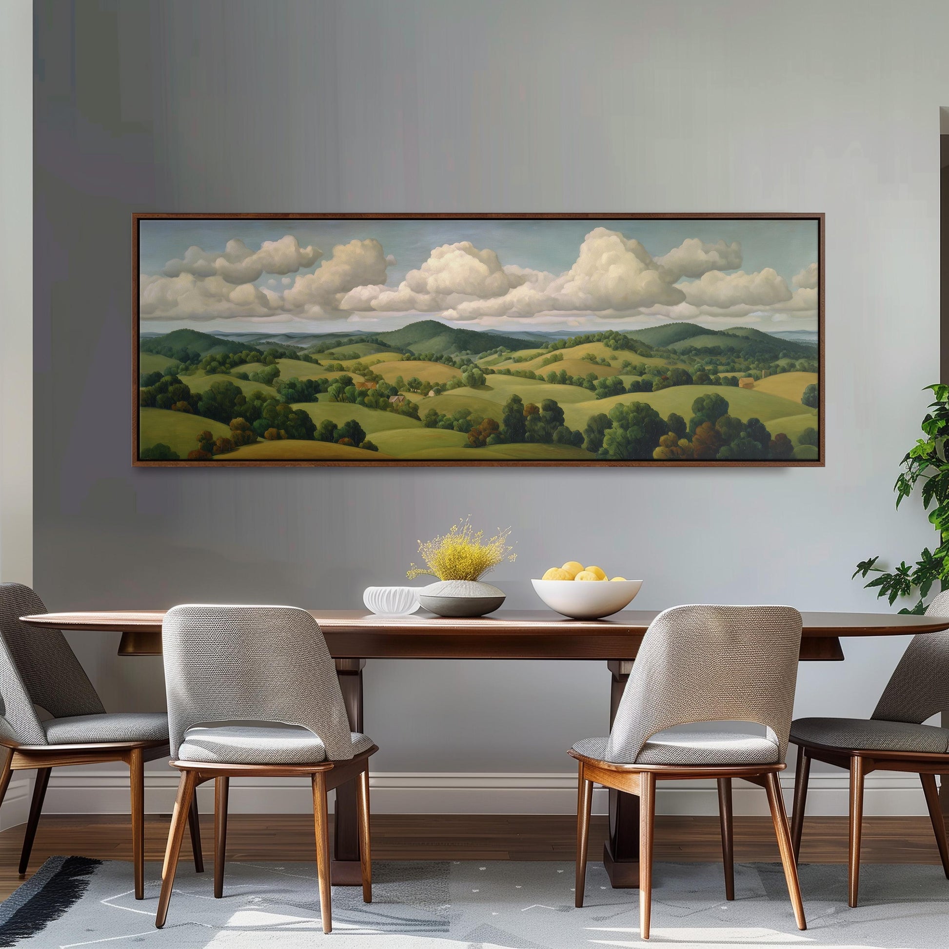a large landscape painting hanging on a wall above a wooden dining table with four chairs. The painting depicts a serene countryside scene with rolling hills, trees, and a cloudy sky.