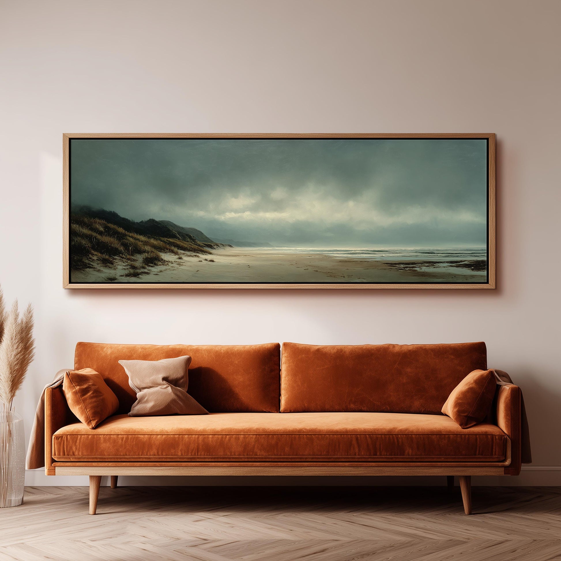 a large, framed painting of a beach scene hanging on a wall above a brown sofa with orange cushions.