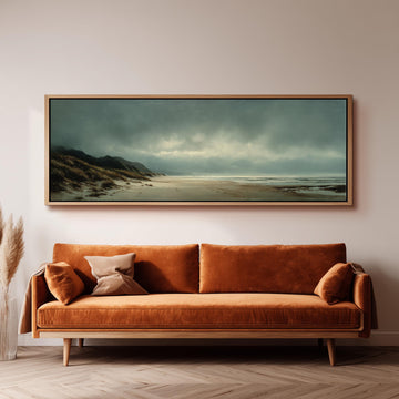 a large, framed painting of a beach scene hanging on a wall above a brown sofa with orange cushions.