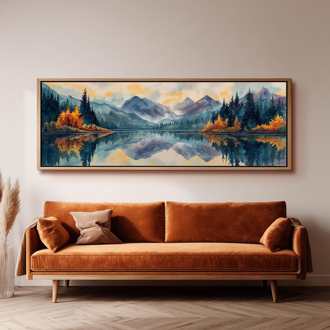 a large, framed painting of a serene landscape with mountains, trees, and a lake, hanging on a wall above a brown sofa.