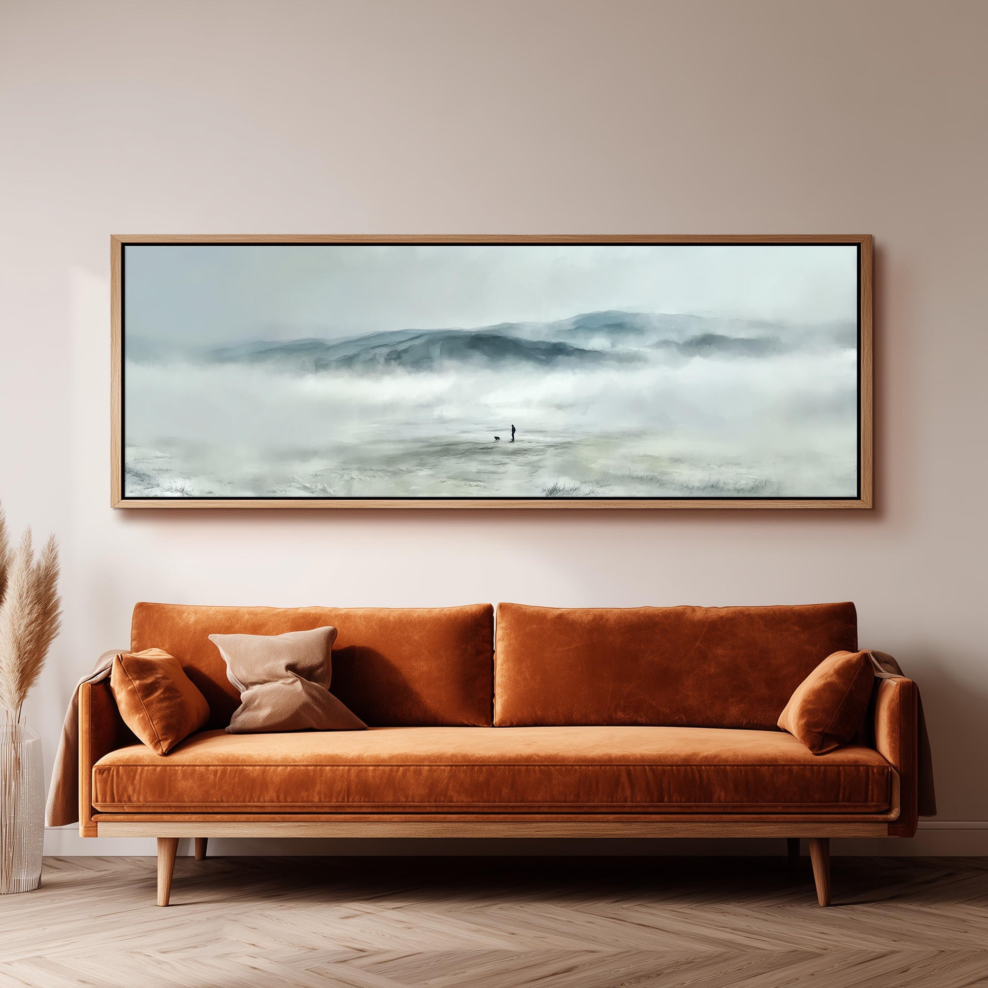a large, framed painting of a misty mountain landscape hanging on a wall above a brown sofa with orange cushions.