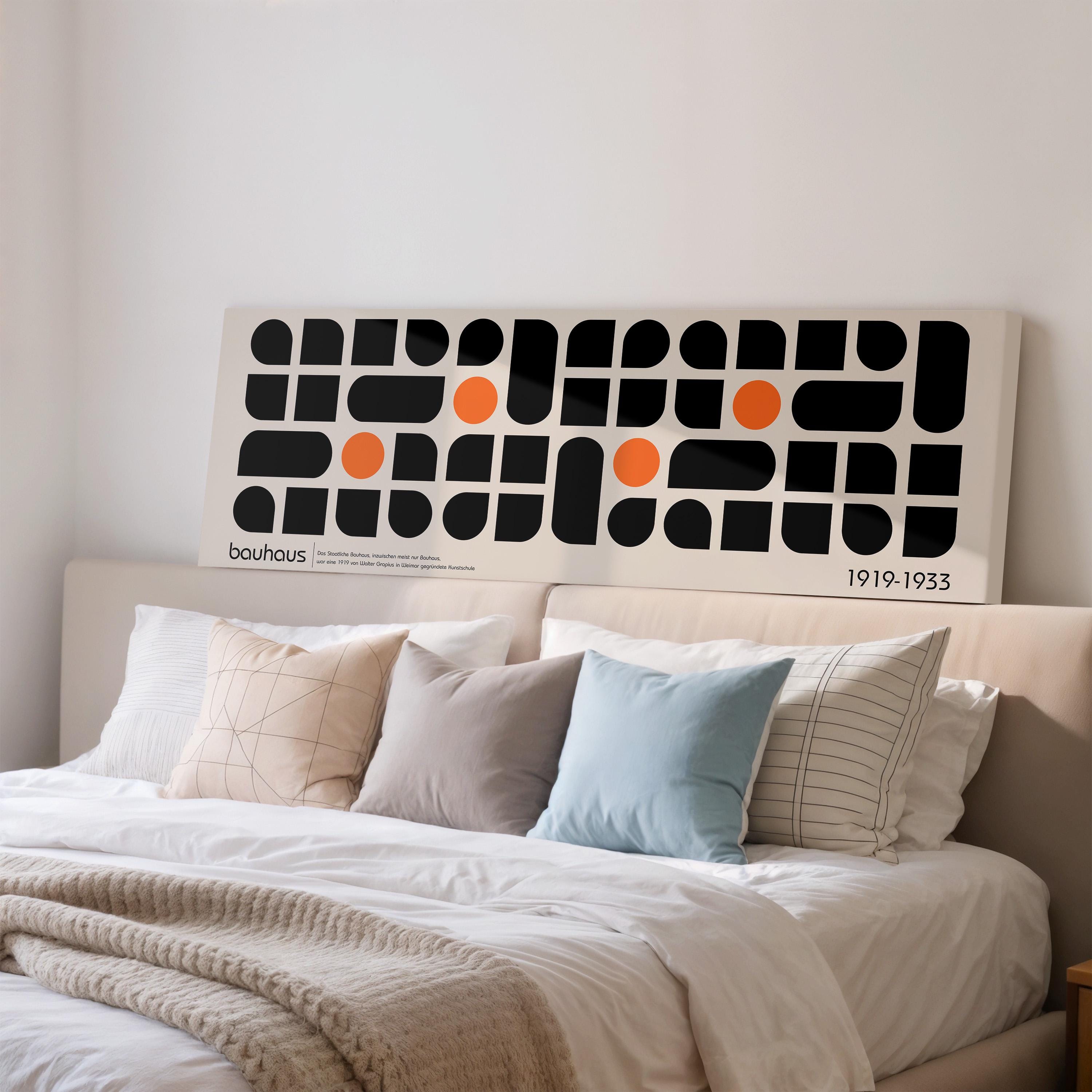 a large abstract art piece with black and orange shapes on a white background, mounted on a wall above a bed with white pillows and a gray blanket.