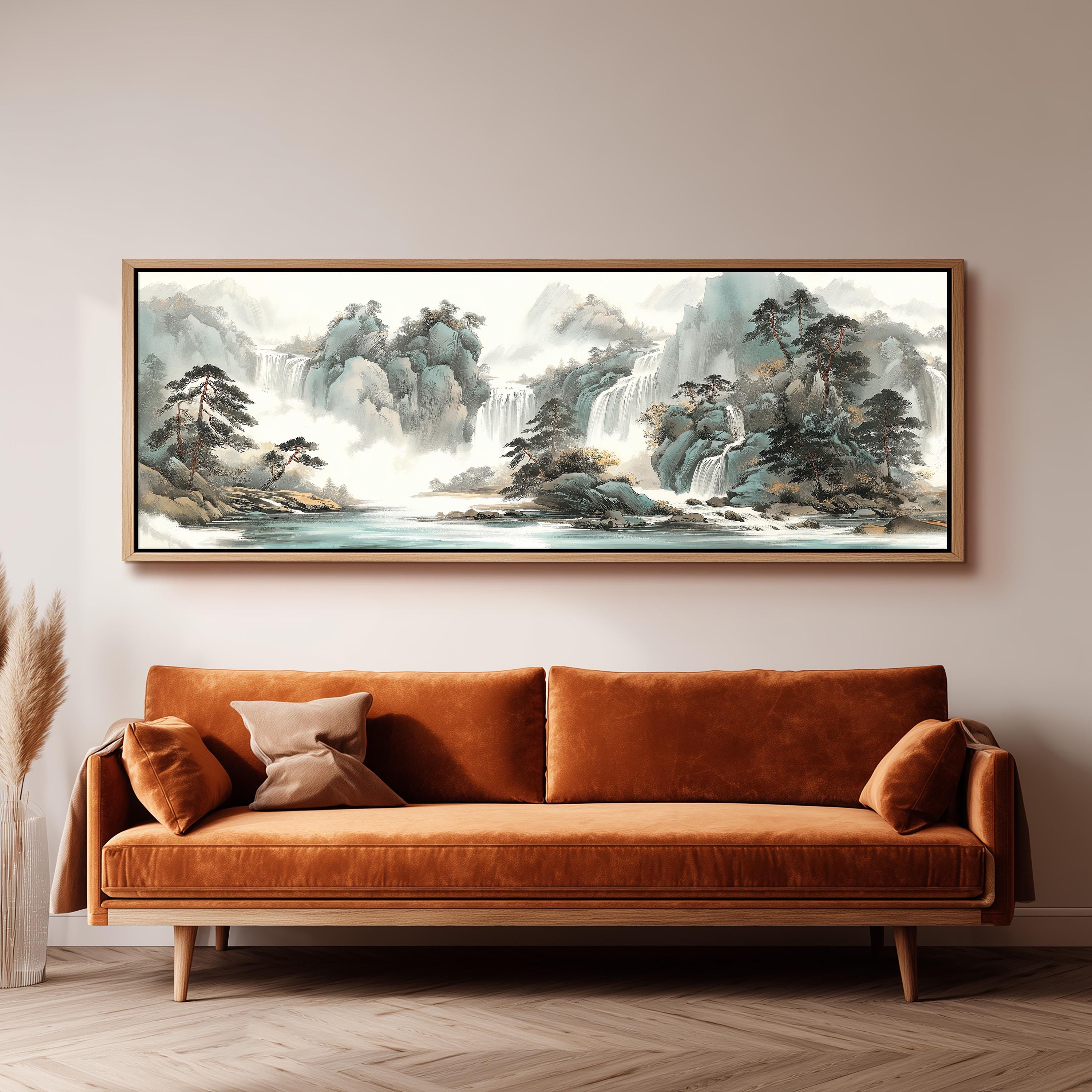a large, framed painting of a serene landscape with mountains, waterfalls, and trees hanging on a wall above a brown sofa.