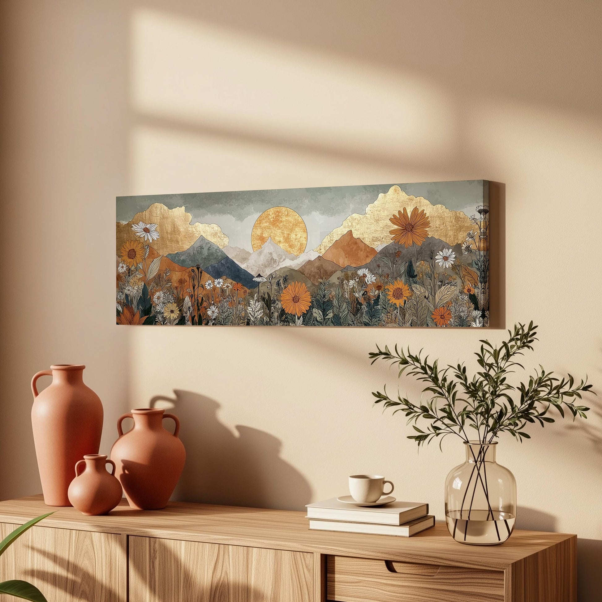 a wooden cabinet with a vase of flowers, a coffee cup, and some books on top of it. Above the cabinet, there is a large painting depicting a mountain landscape with a sun and flowers.