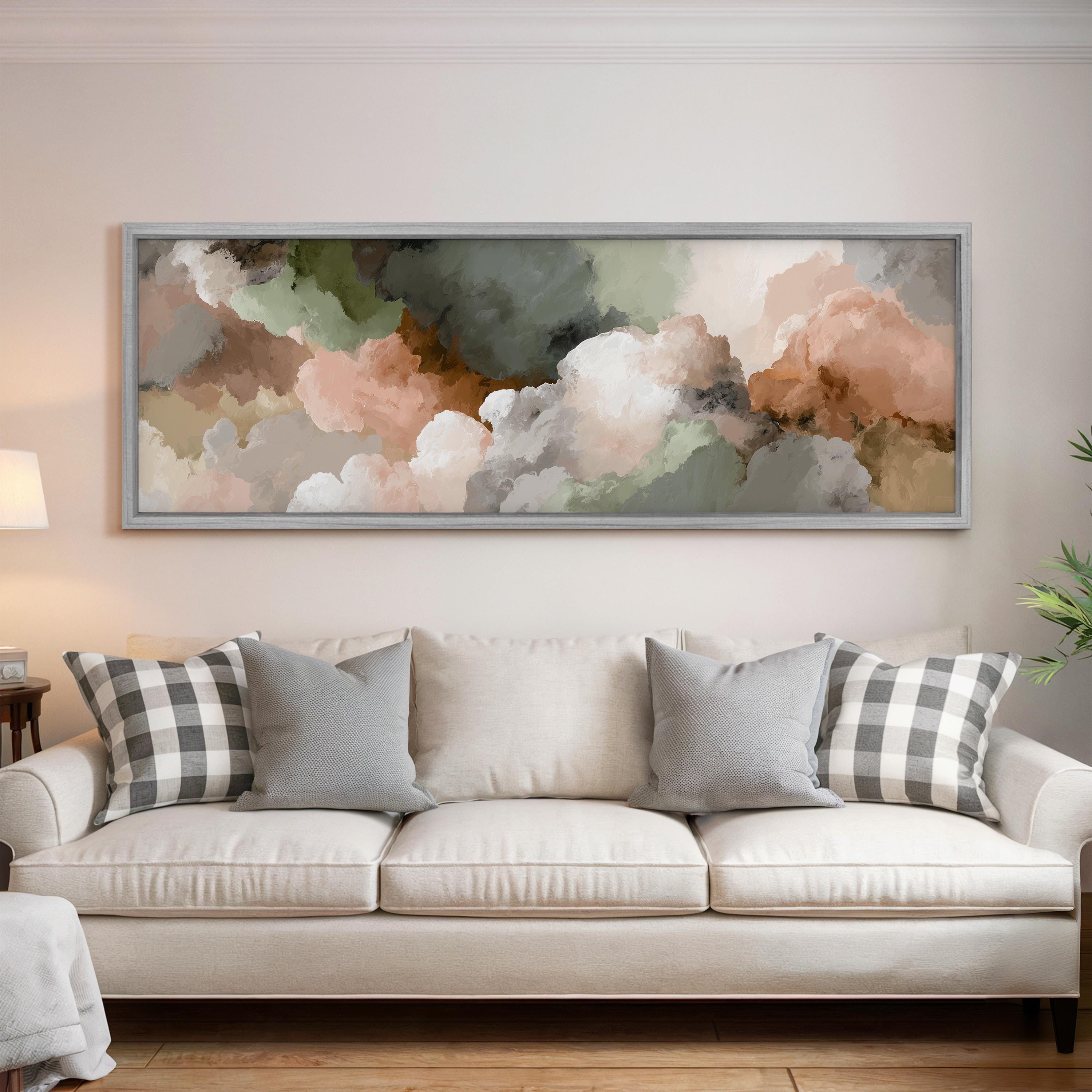 a large, framed painting of clouds hanging above a white couch with gray and white plaid throw pillows.