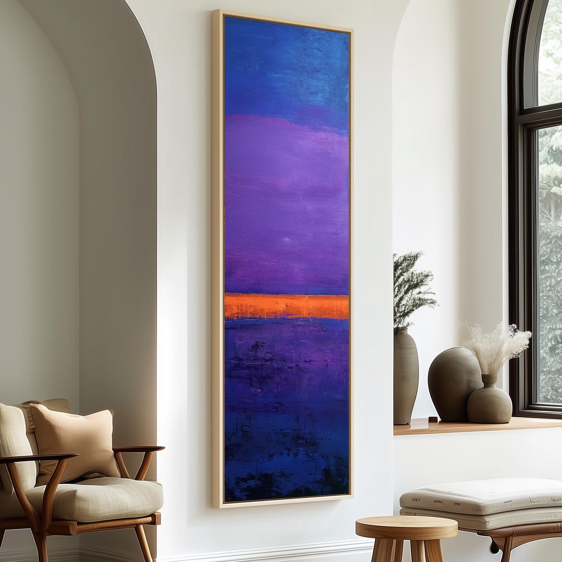 a large abstract painting with a vibrant mix of blue, purple, and orange colors, hanging on a white wall. The painting is framed and appears to be the focal point of the room. In the foreground, there is a wooden chair and a small table with a vase on it. The room also has a window and a plant, adding to the overall aesthetic of the space.