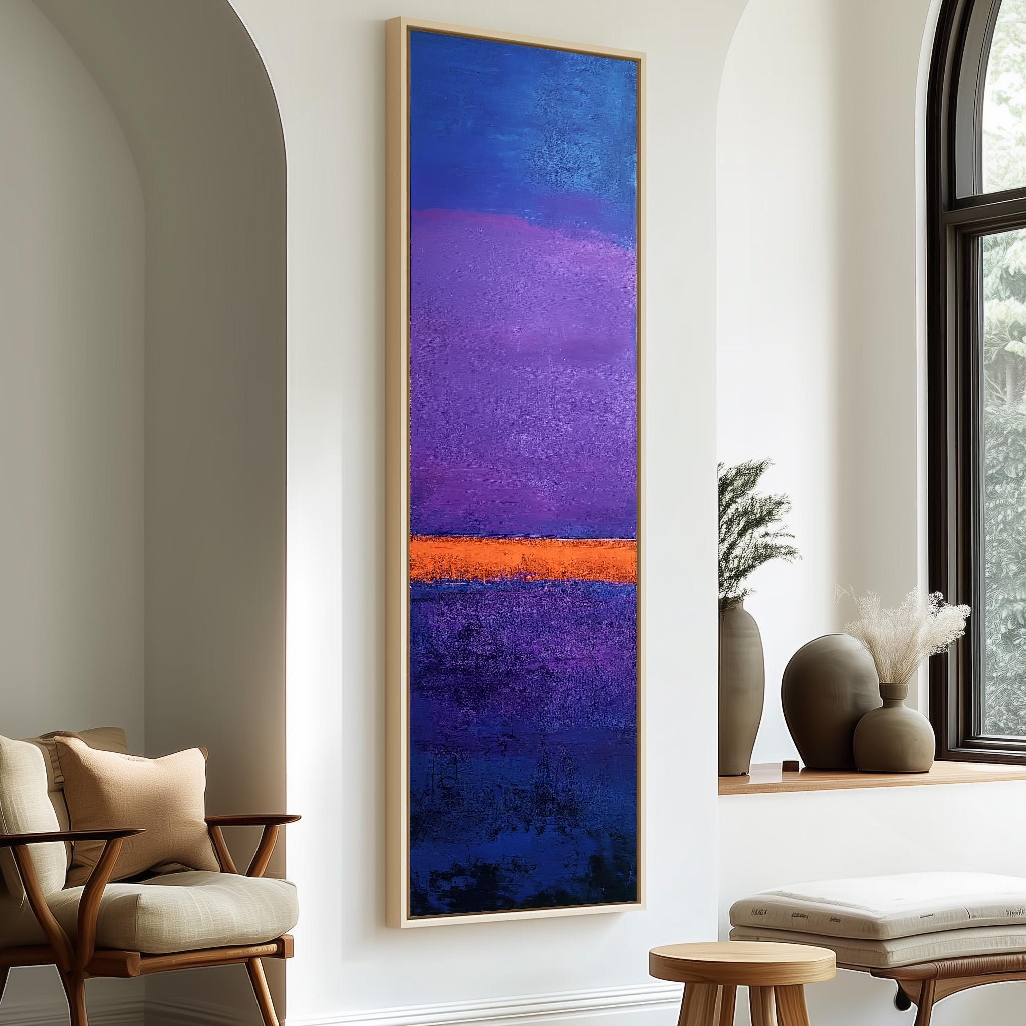 a large abstract painting with a vibrant mix of blue, purple, and orange colors, hanging on a white wall. The painting is framed and appears to be the focal point of the room. In the foreground, there is a wooden chair and a small table with a vase on it. The room also has a window and a plant, adding to the overall aesthetic of the space.