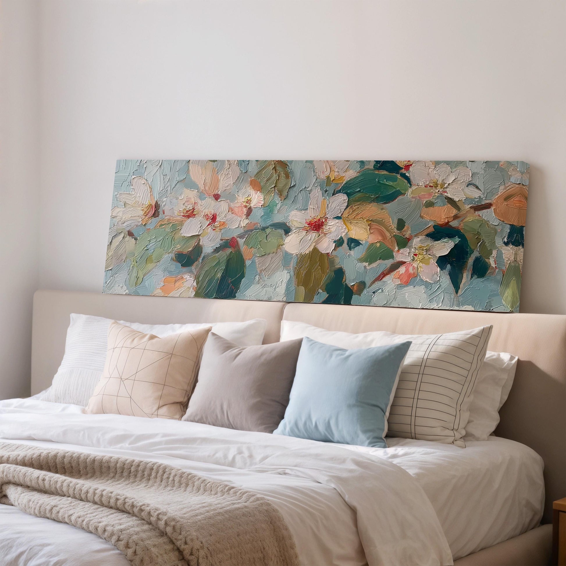 a large floral painting hanging above a bed with white pillows and a gray blanket.