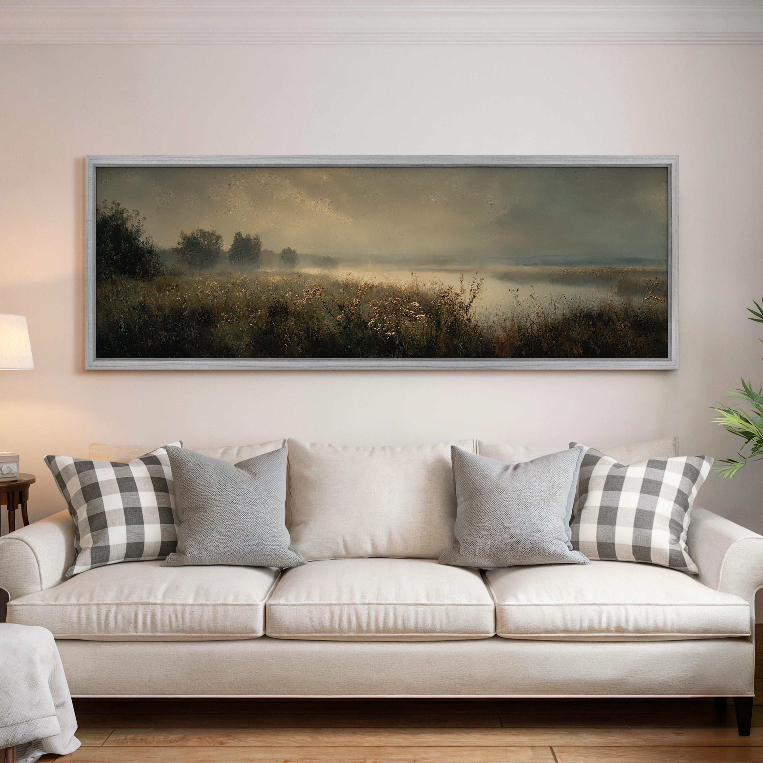 a large, framed landscape painting hanging on a wall above a white sofa with gray and white patterned throw pillows.