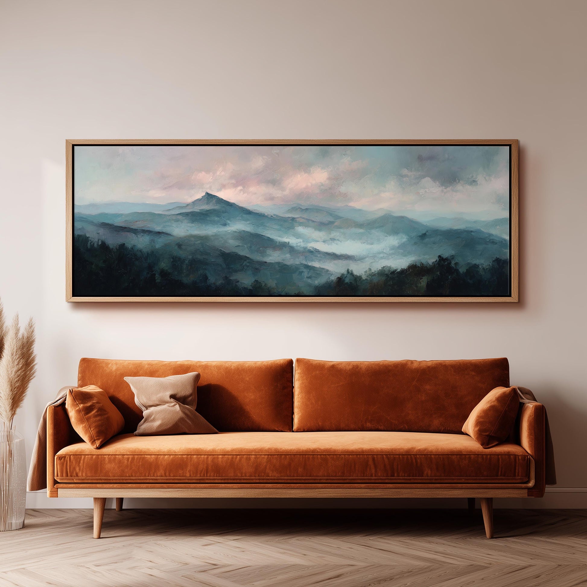 a large, framed painting of a mountain landscape hanging on a wall above a brown sofa with orange cushions.
