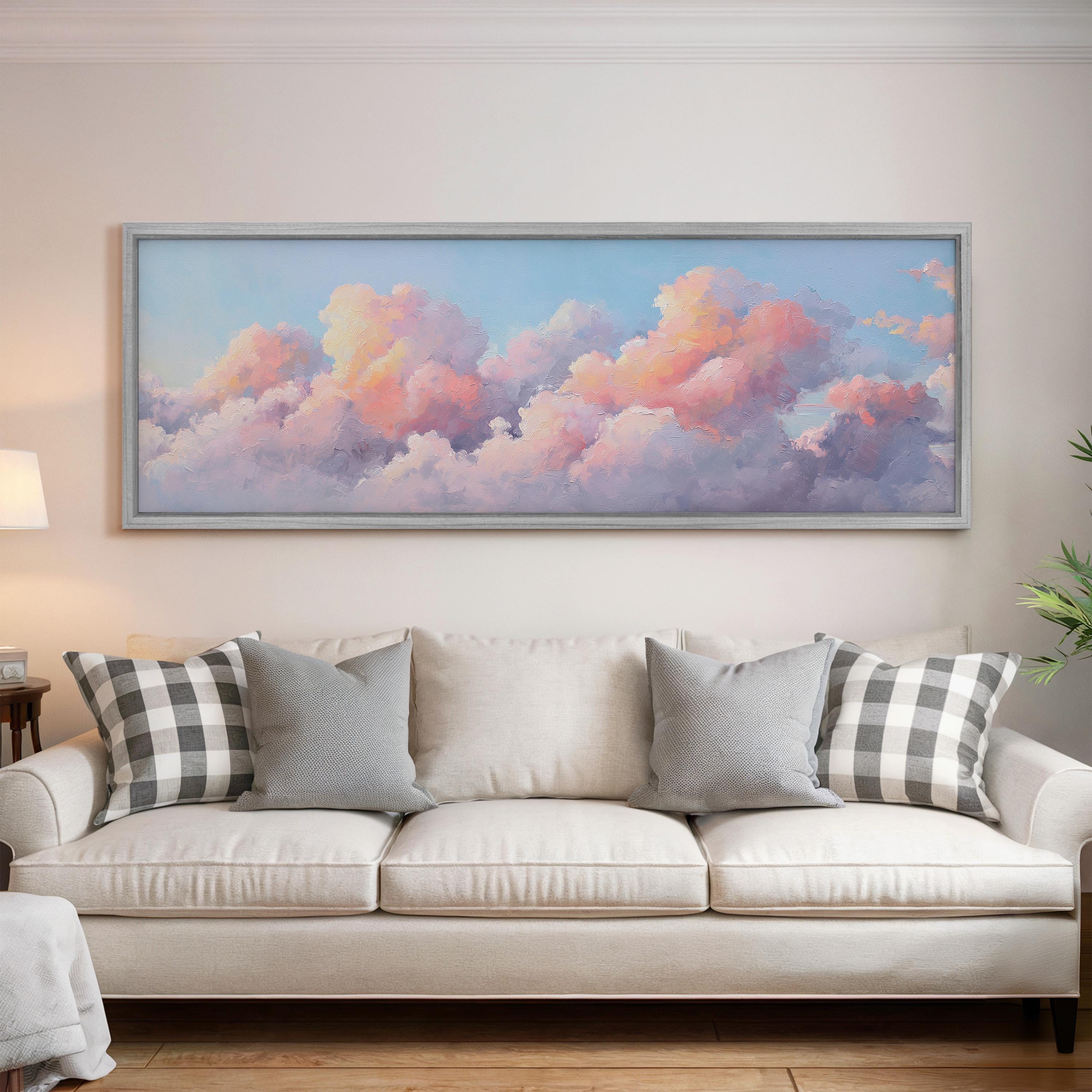a large, framed painting of a cloudy sky hanging on a wall above a white couch with gray and black plaid throw pillows.