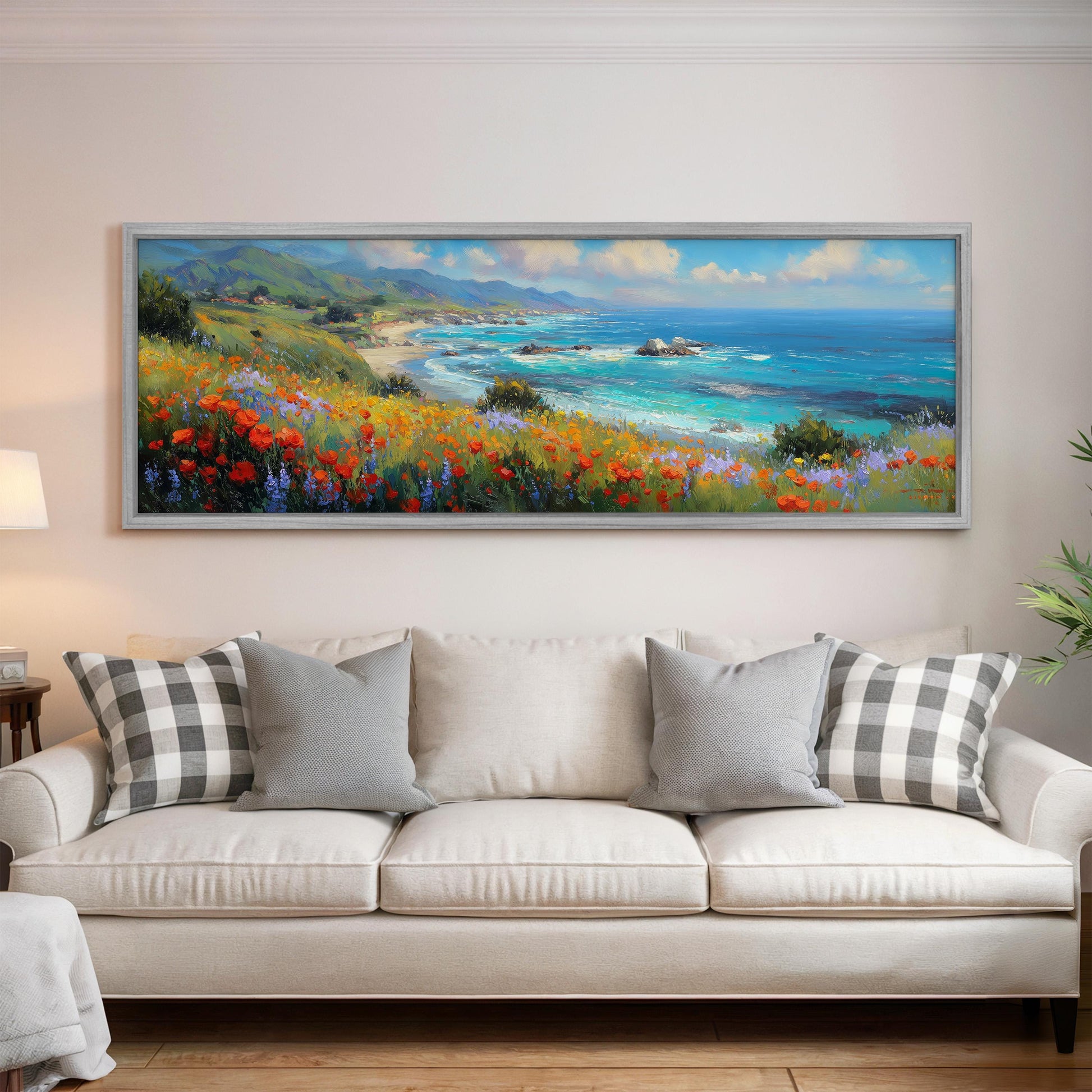 a large, framed painting of a coastal landscape hanging on a wall above a white sofa with gray and white patterned pillows.