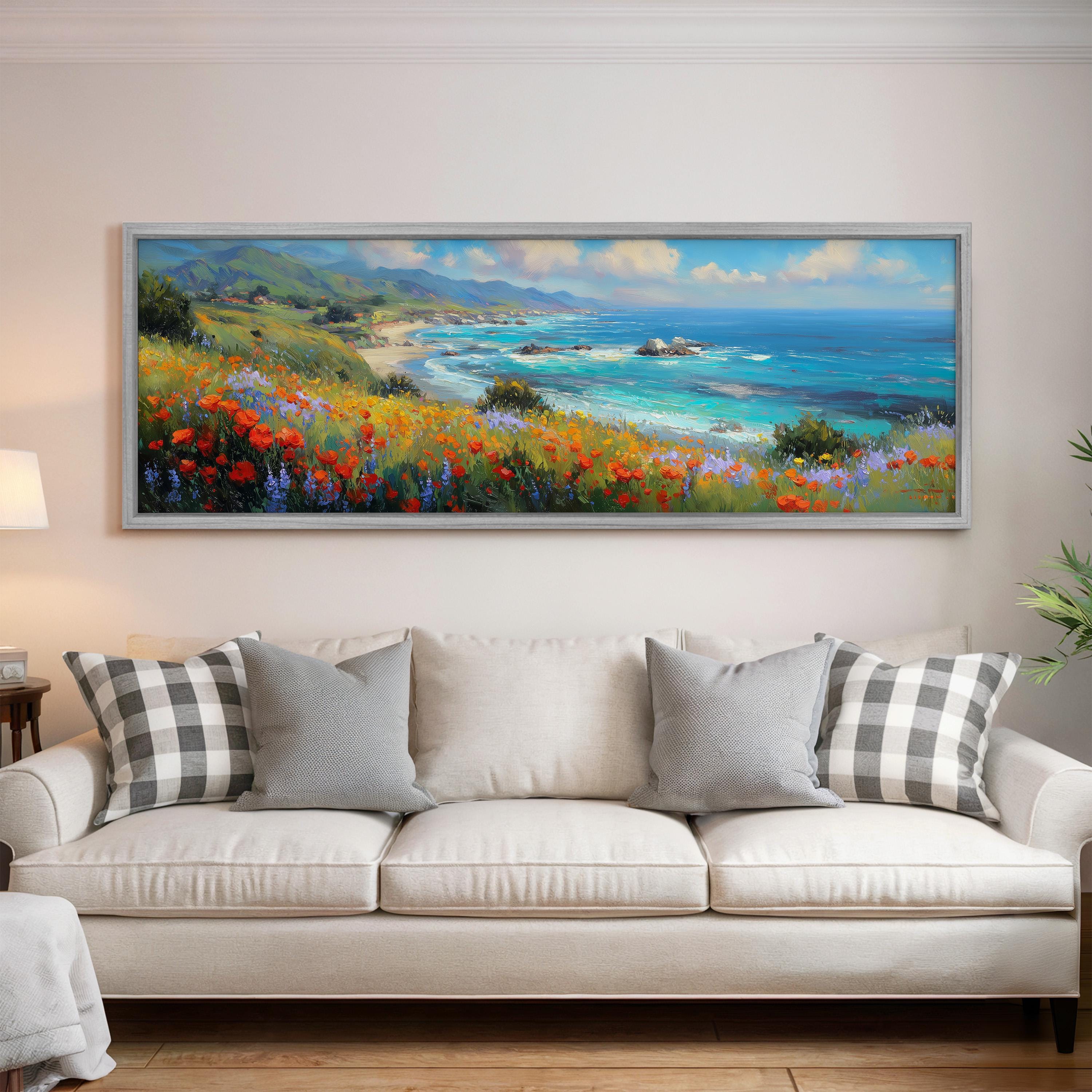 a large, framed painting of a coastal landscape hanging on a wall above a white sofa with gray and white patterned pillows.
