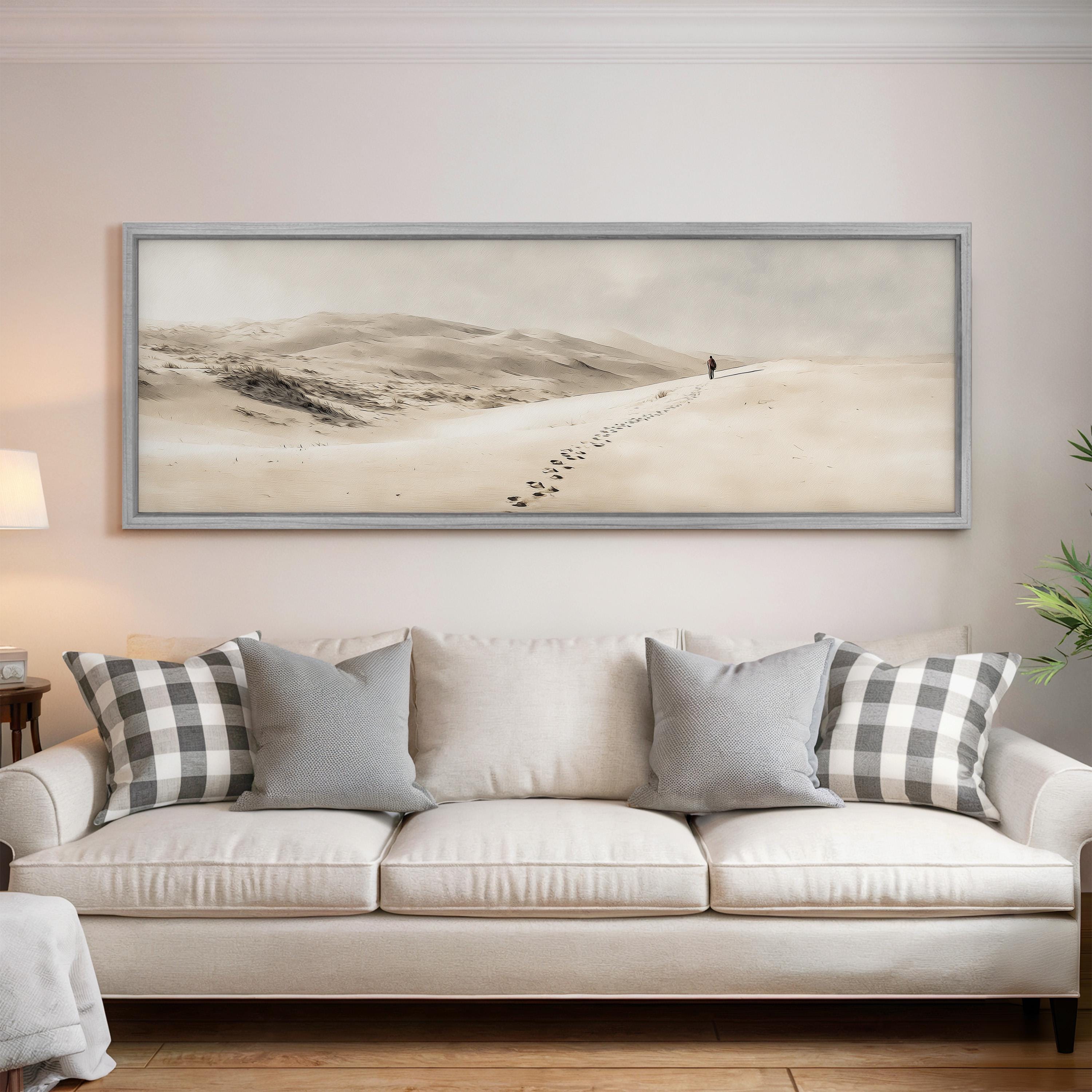 a large framed picture of a person walking on a snowy path, with a dog following behind, hanging on a wall above a white couch with patterned throw pillows.