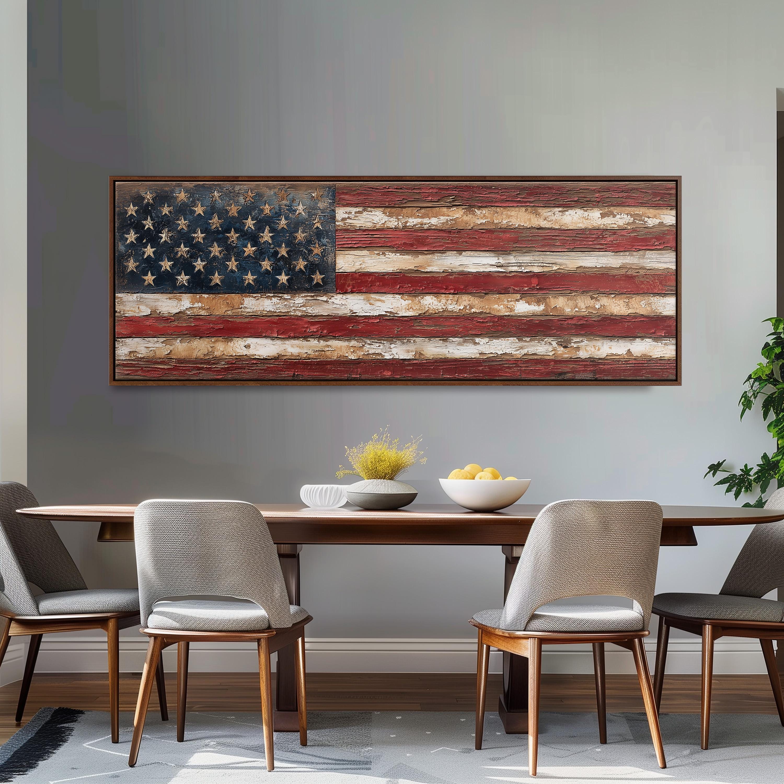 a dining room with a large American flag displayed on the wall above a wooden table with four chairs. The table is set with a bowl of fruit and a vase of flowers, creating a welcoming and patriotic atmosphere.