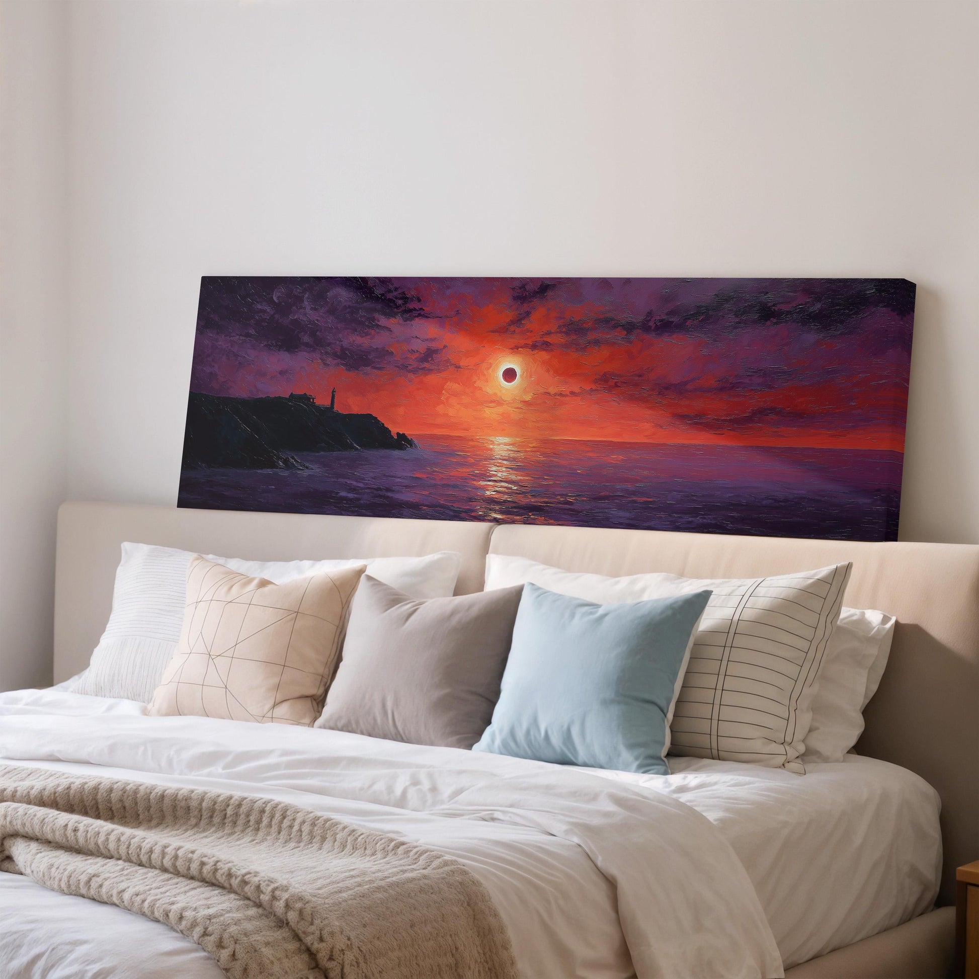a large painting of a sunset over the ocean, hanging on a wall above a bed with white pillows and a gray blanket.