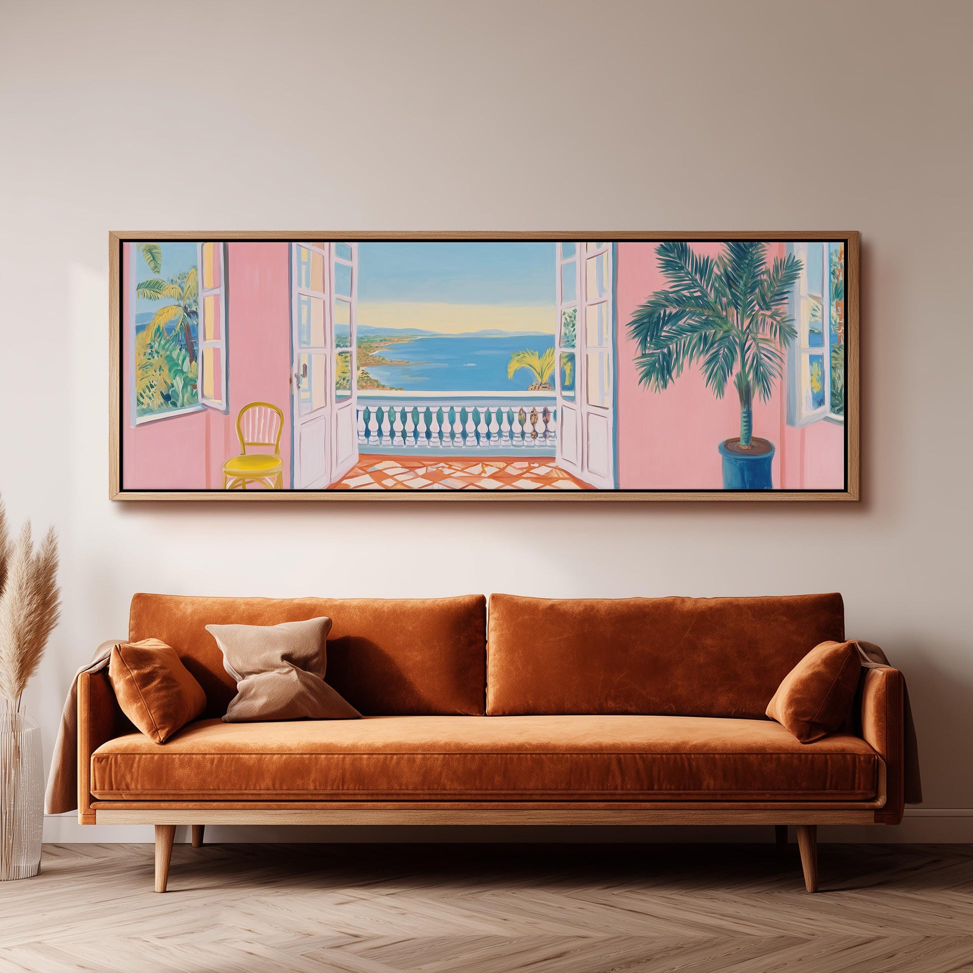 a large, colorful painting of a balcony overlooking the ocean, with a palm tree and a pink wall in the background. The painting is hung on a wall above a brown sofa, creating a cozy and inviting atmosphere in the room.