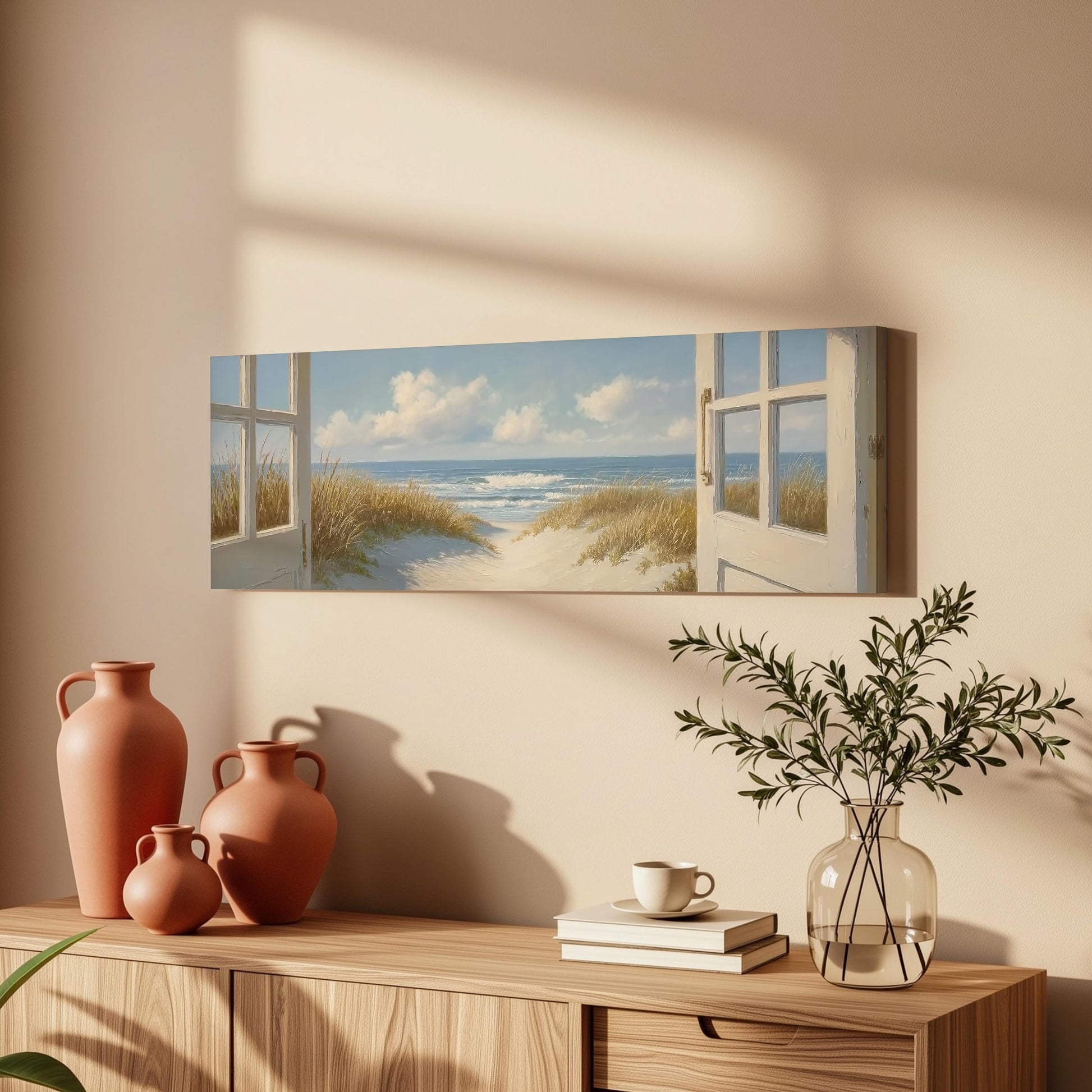a serene beach scene with a painting of a beach view, a vase with greenery, and a wooden dresser with books and a coffee cup.