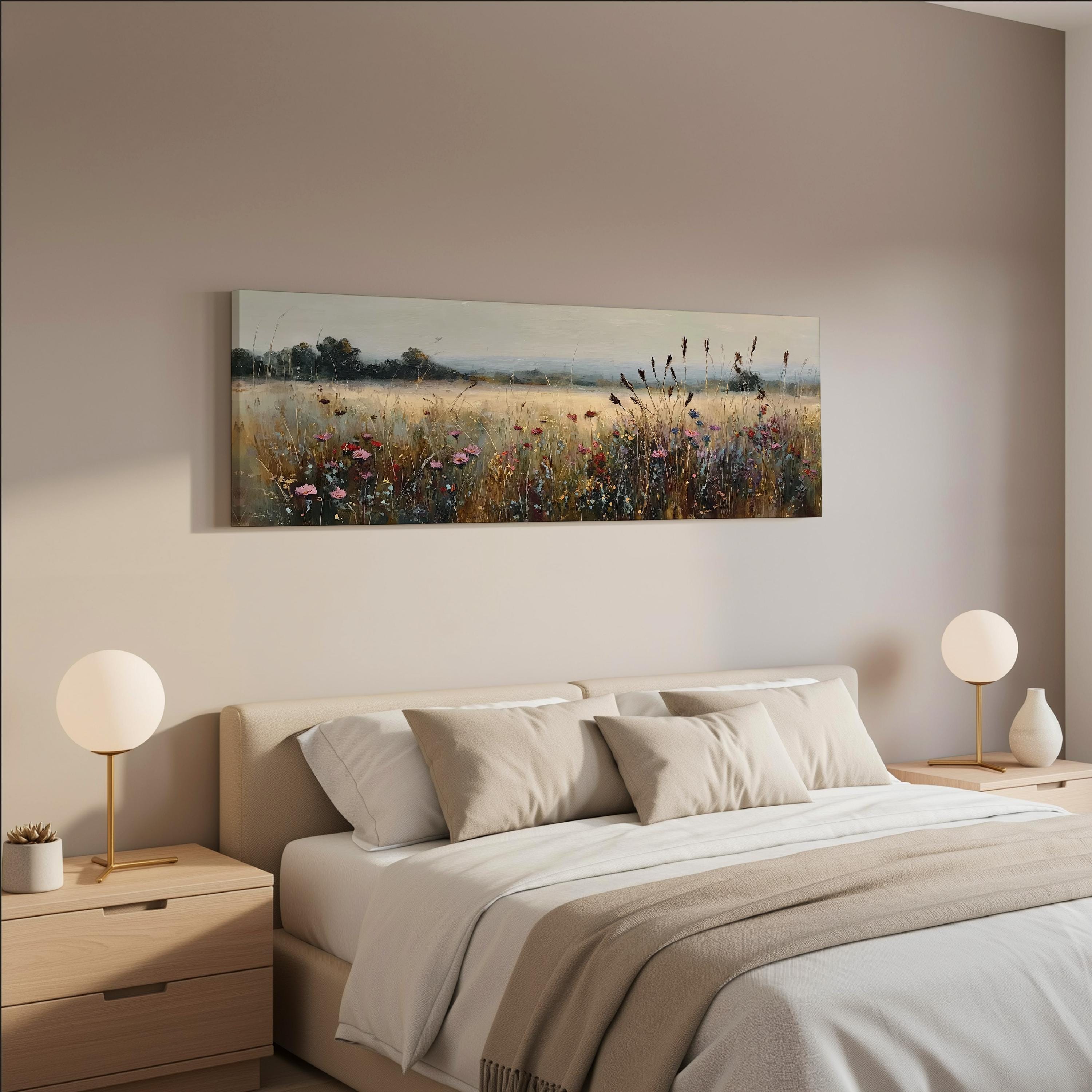 a serene bedroom scene with a large bed adorned with white linens and beige throw pillows. Above the bed, a painting of a field with wildflowers is displayed on the wall, creating a peaceful and natural atmosphere. The room is well-lit, with two round table lamps on either side of the bed providing soft, ambient lighting.